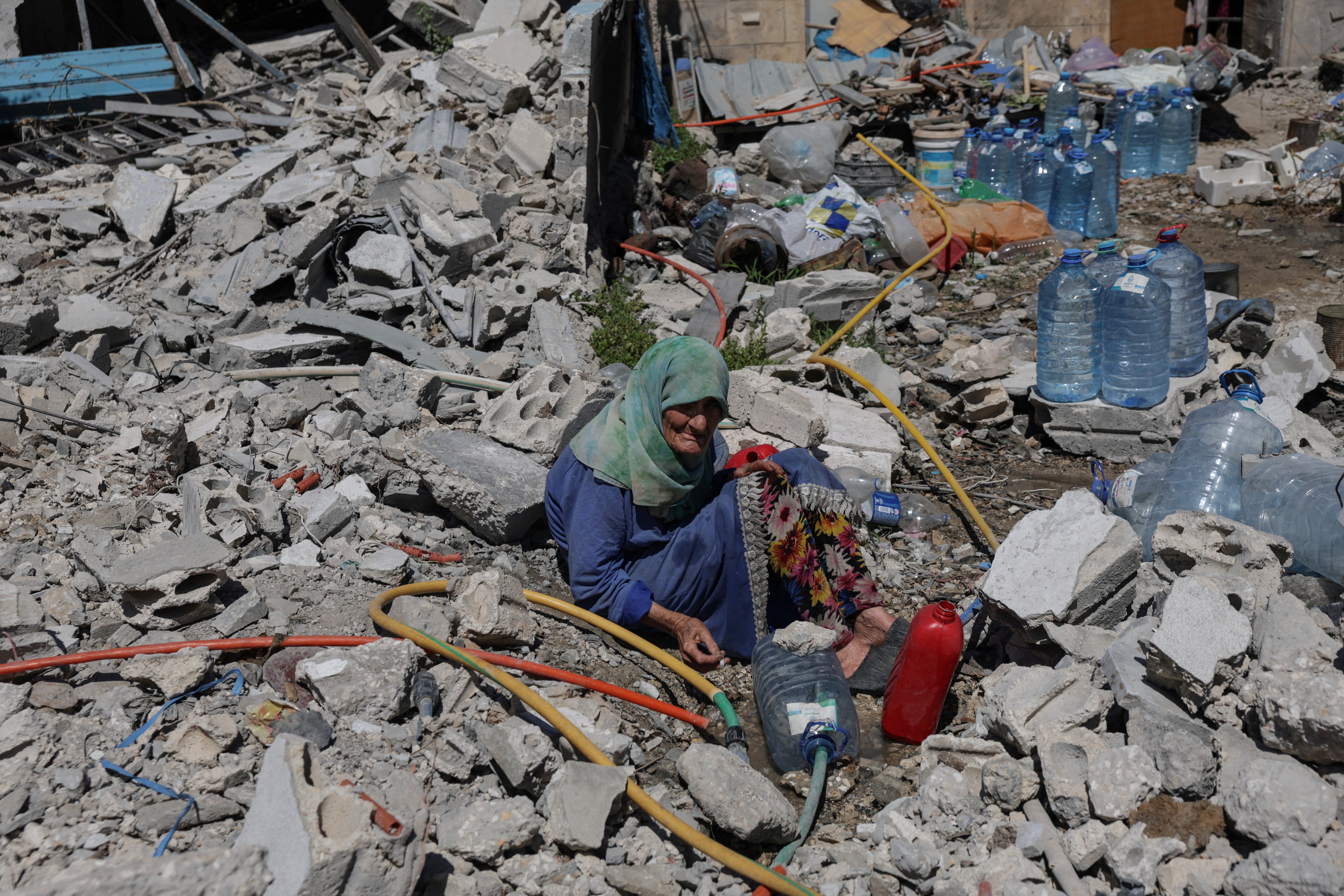 Khadija Amara, whom local residents said had not left her home, fills a jerrycan with water as she sits among the rubble of a house, which was damaged by an Israeli strike, in Qlaileh in the Tyre district, southern Lebanon