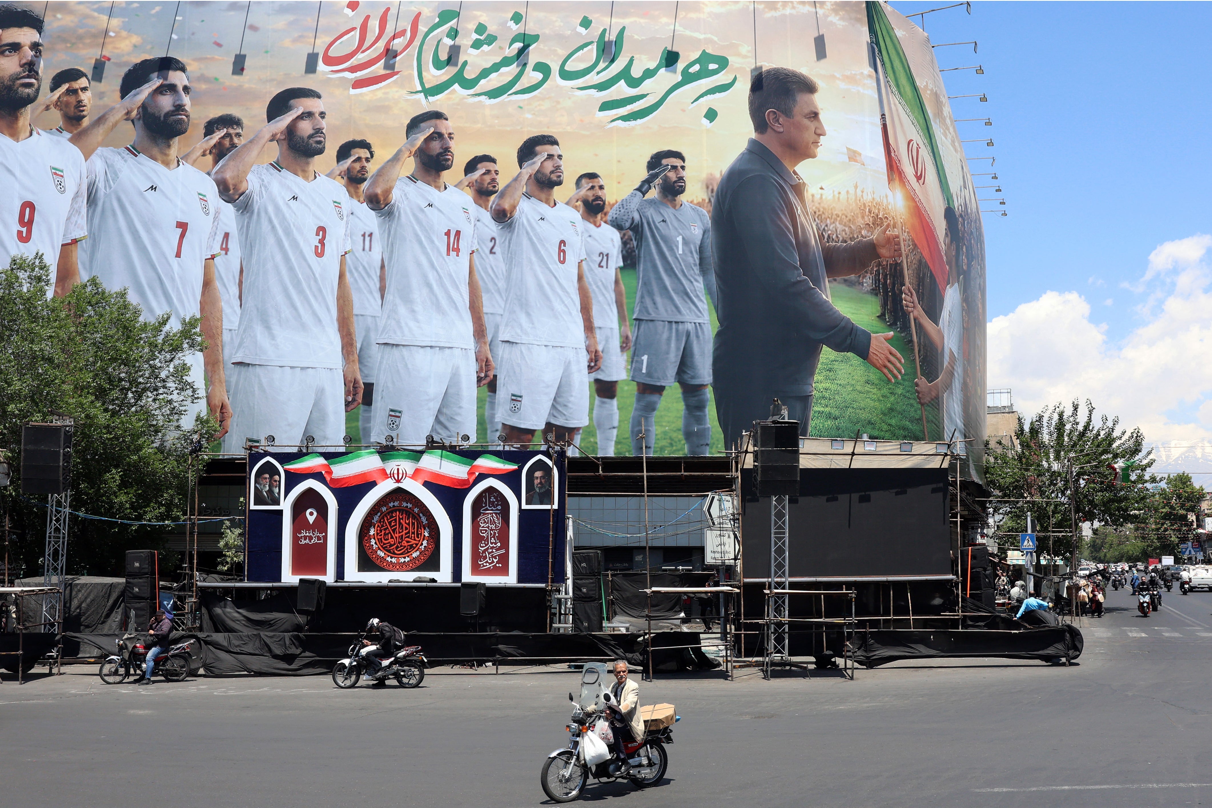 People on motorbikes ride past a billboard supporting Iran's national football team in Tehran (AFP/Getty)