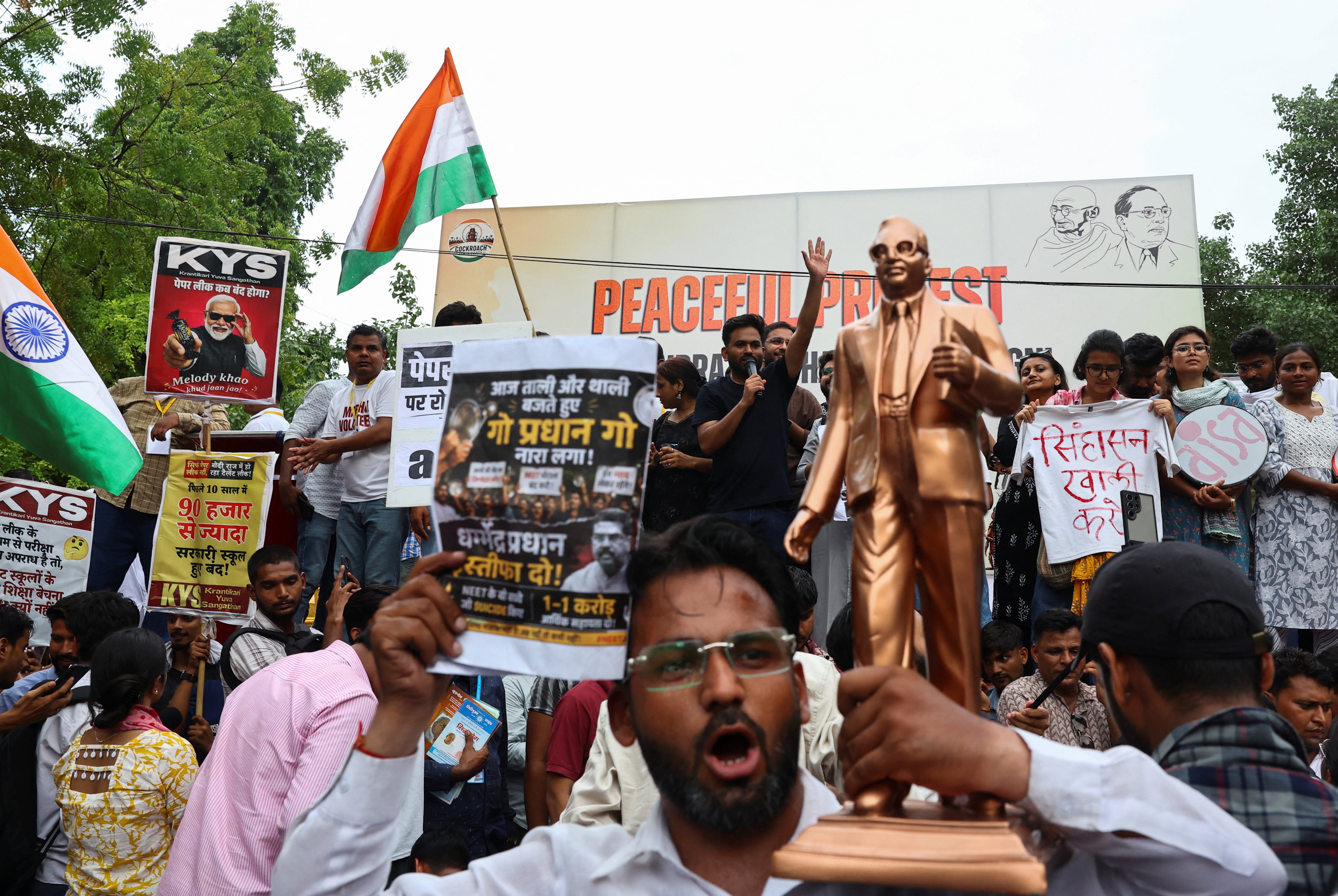 People hold placards and shout slogans as Abhijeet Dipke, head of the CJP, waves to the crowd during a sit-in protest demanding the resignation of Indian education minister Dharmendra Pradhan