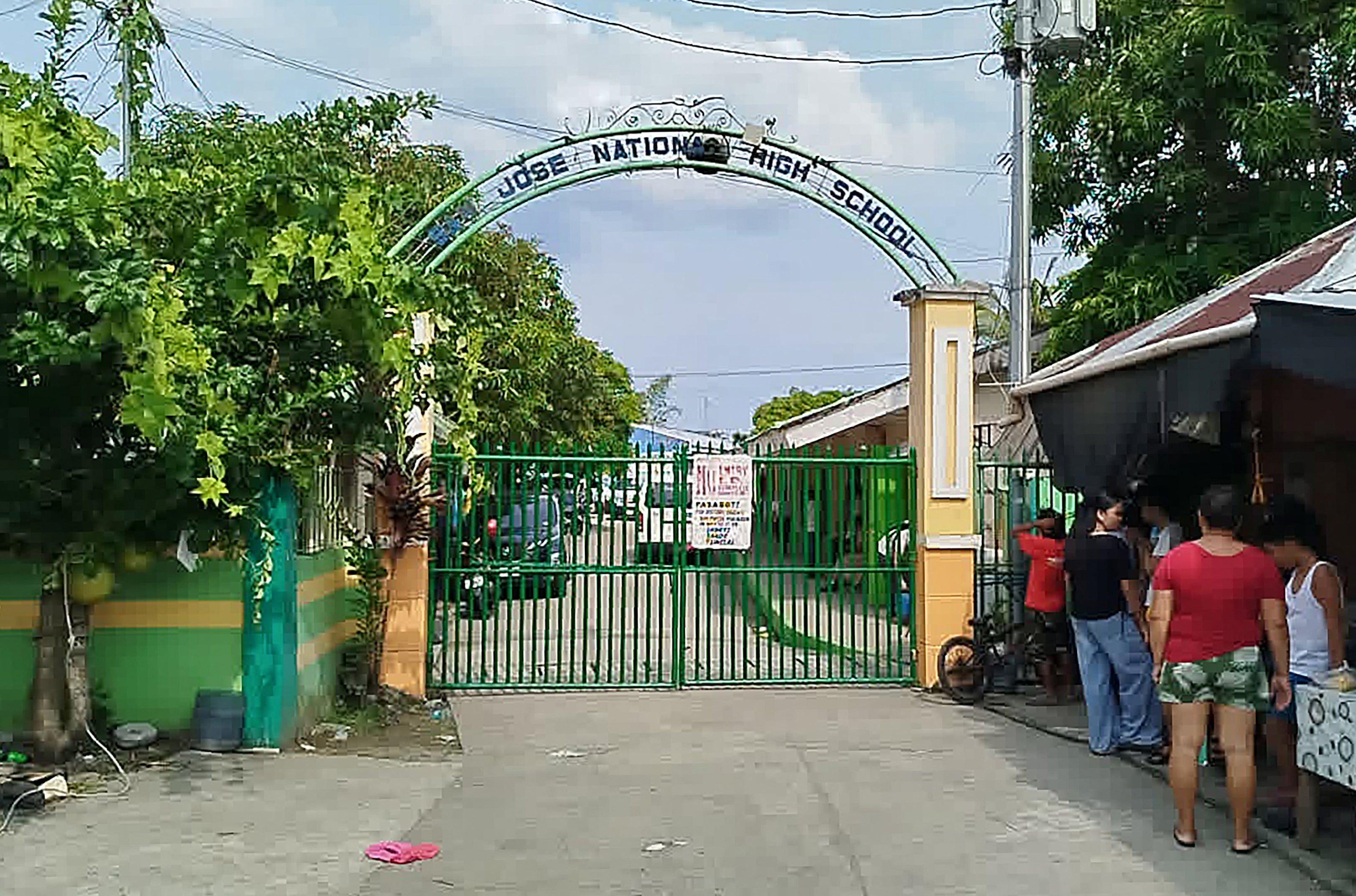 People stand next to the entrance gate of San Jose National High School after a shooting incident in Tacloban City, Leyte province on June 22, 2026