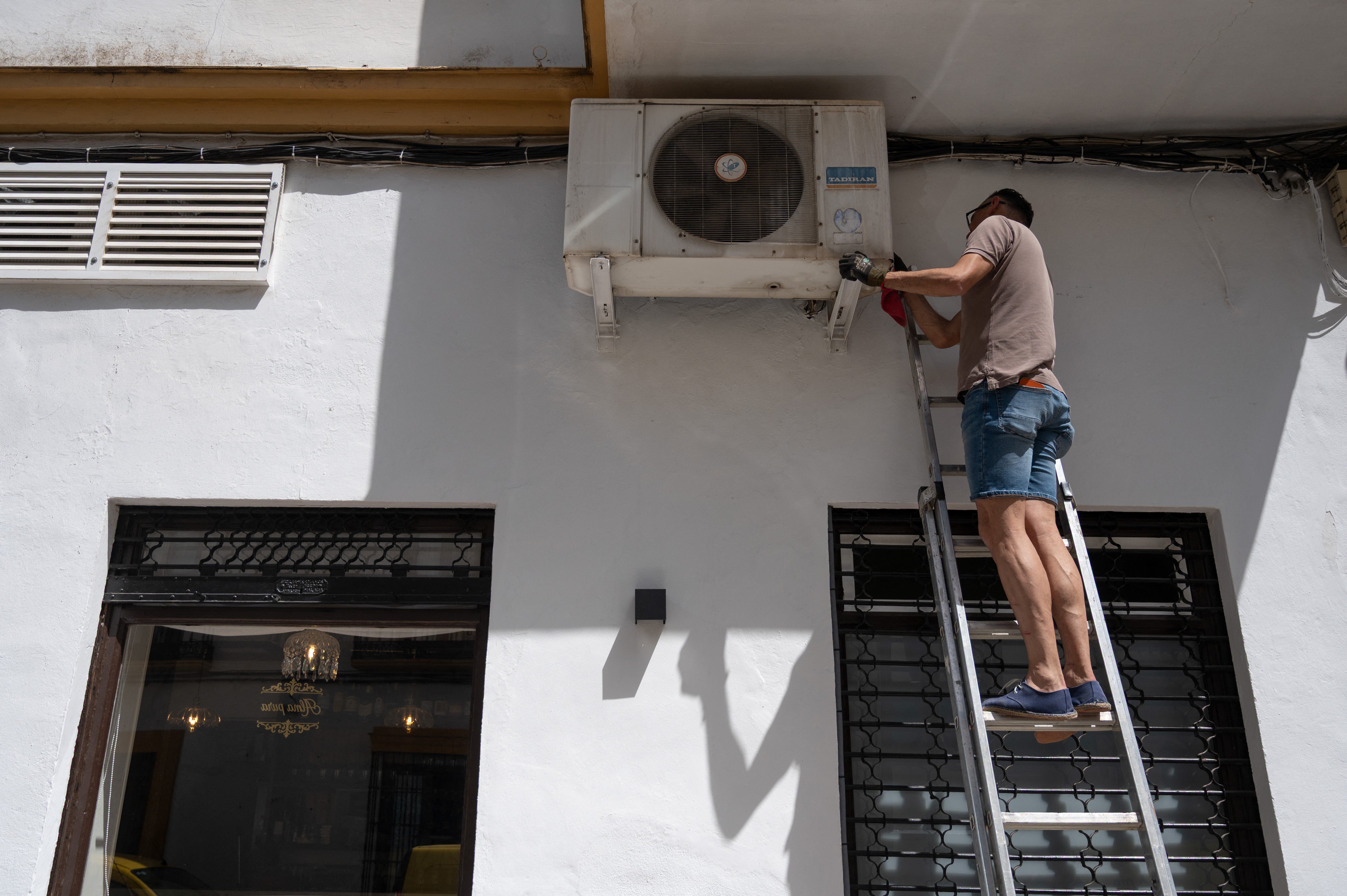 A technician repairs an air conditioner on the facade of a restaurant in the city centre of Ronda in southern Spain