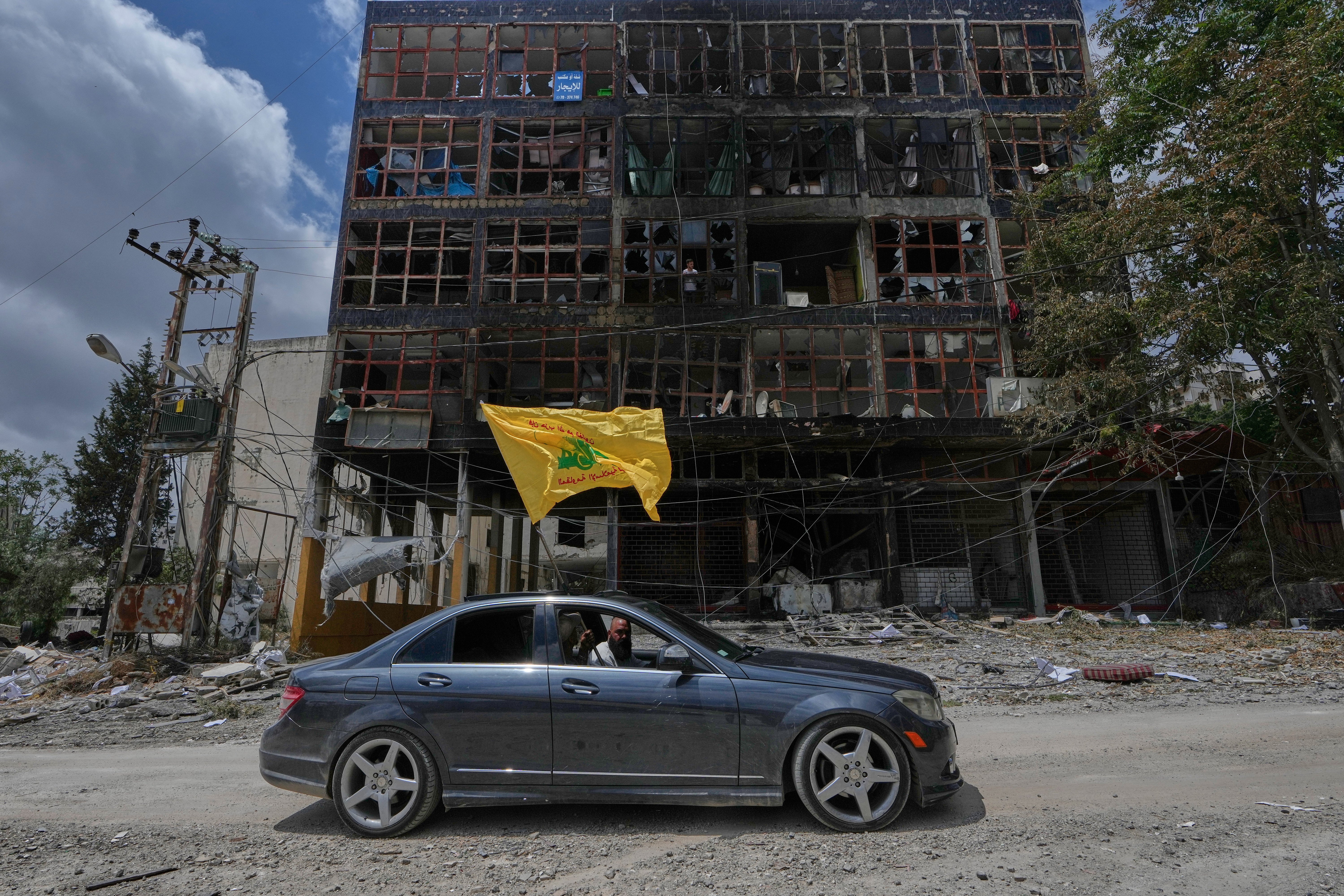 A man with a Hezbollah flag drives past a damaged building in Nabatiyeh, southern Lebanon, which has been devastated by Israeli airstrikes (AP)