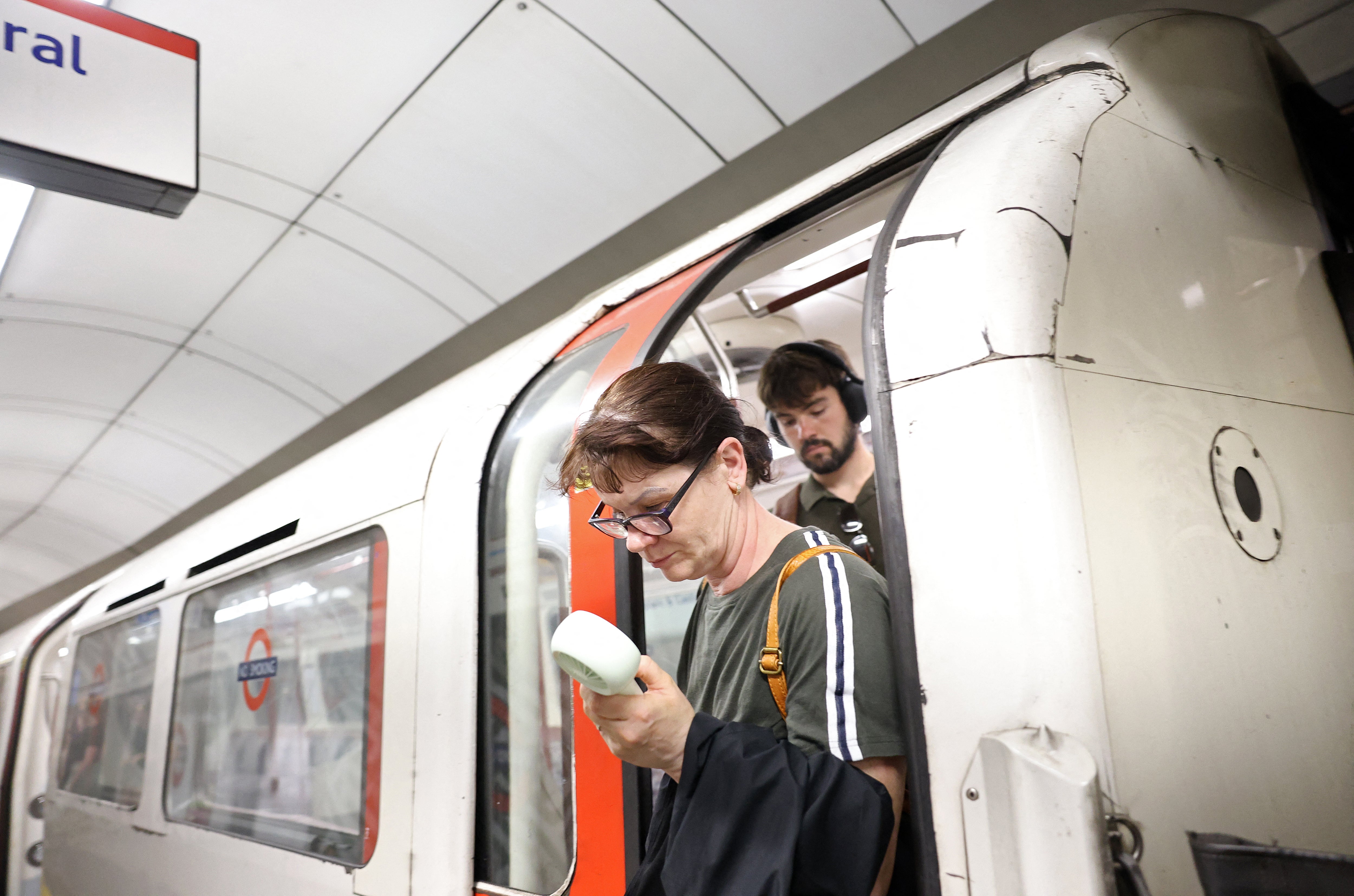 A commuter uses a fan in an attempt to cool down, as they exit a London Underground tube carriage, in London on 23 June 2026