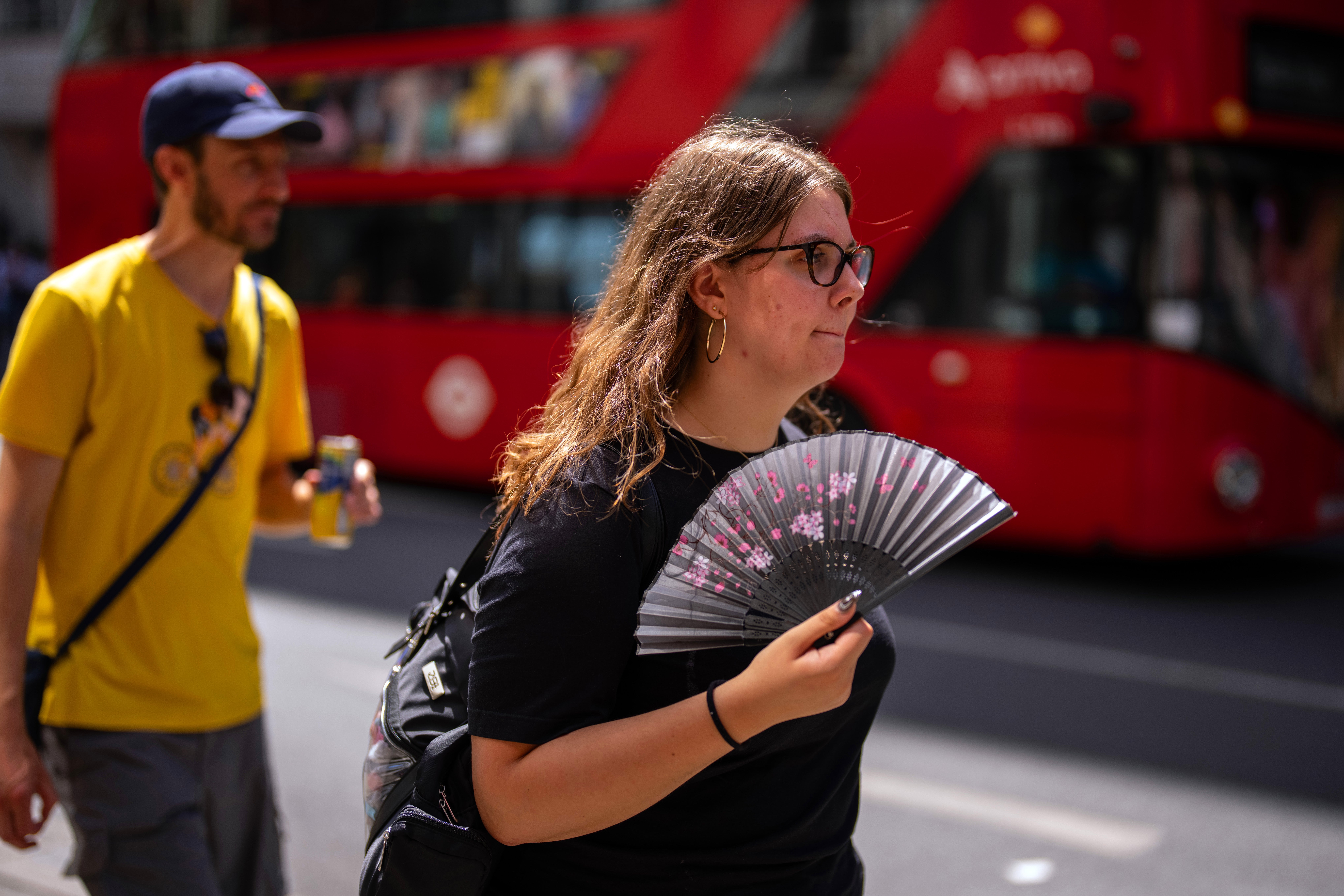 A woman uses a fan to cool herself as she walks through central London in the hot weather (Getty)