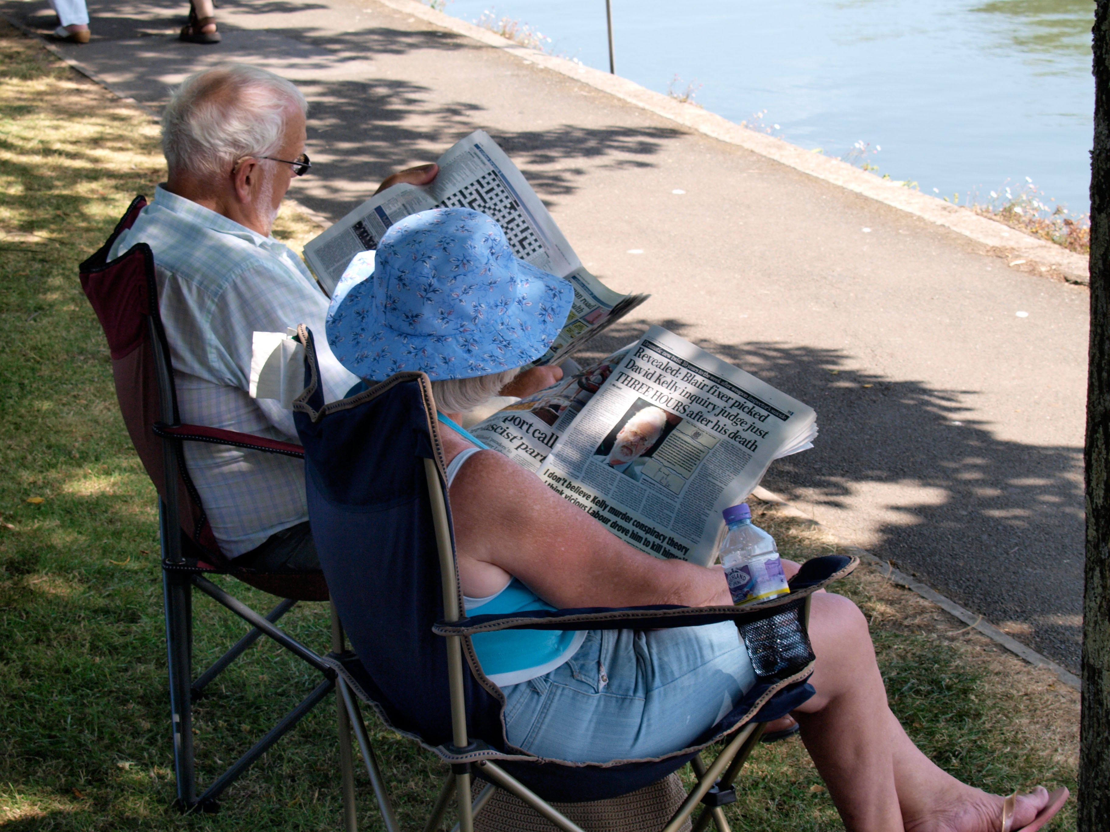 Old couple sitting in the shade of a tree reading newspapers (Alamy/PA)