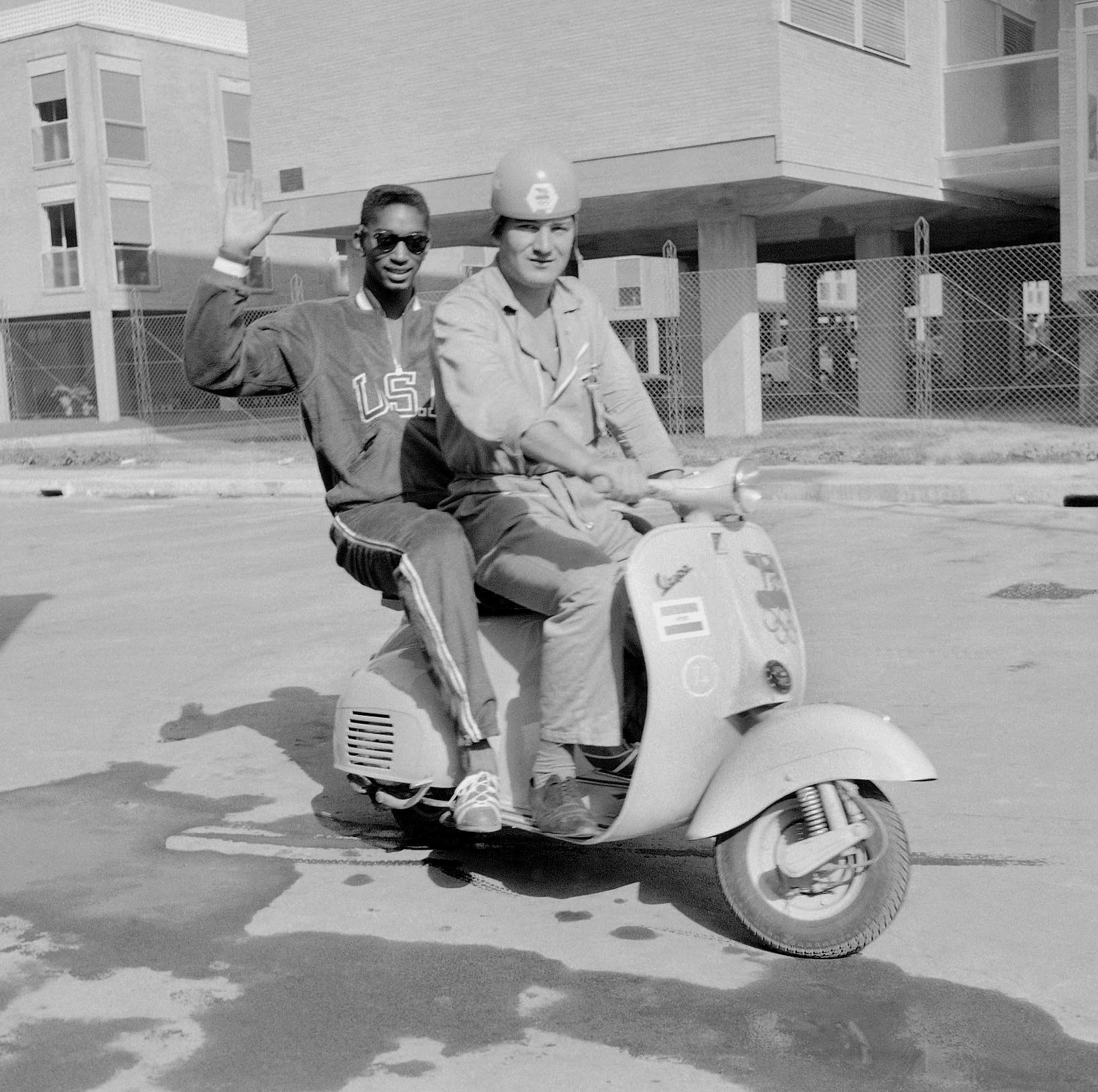 FILE - U.S. high jumper John Thomas, of Cambridge, Mass., waves from a Vespa scooter with an unidentified official Olympic driver inside the Olympic Village, in Rome, Aug. 27, 1960. (AP Photo/Mike Stern, File)