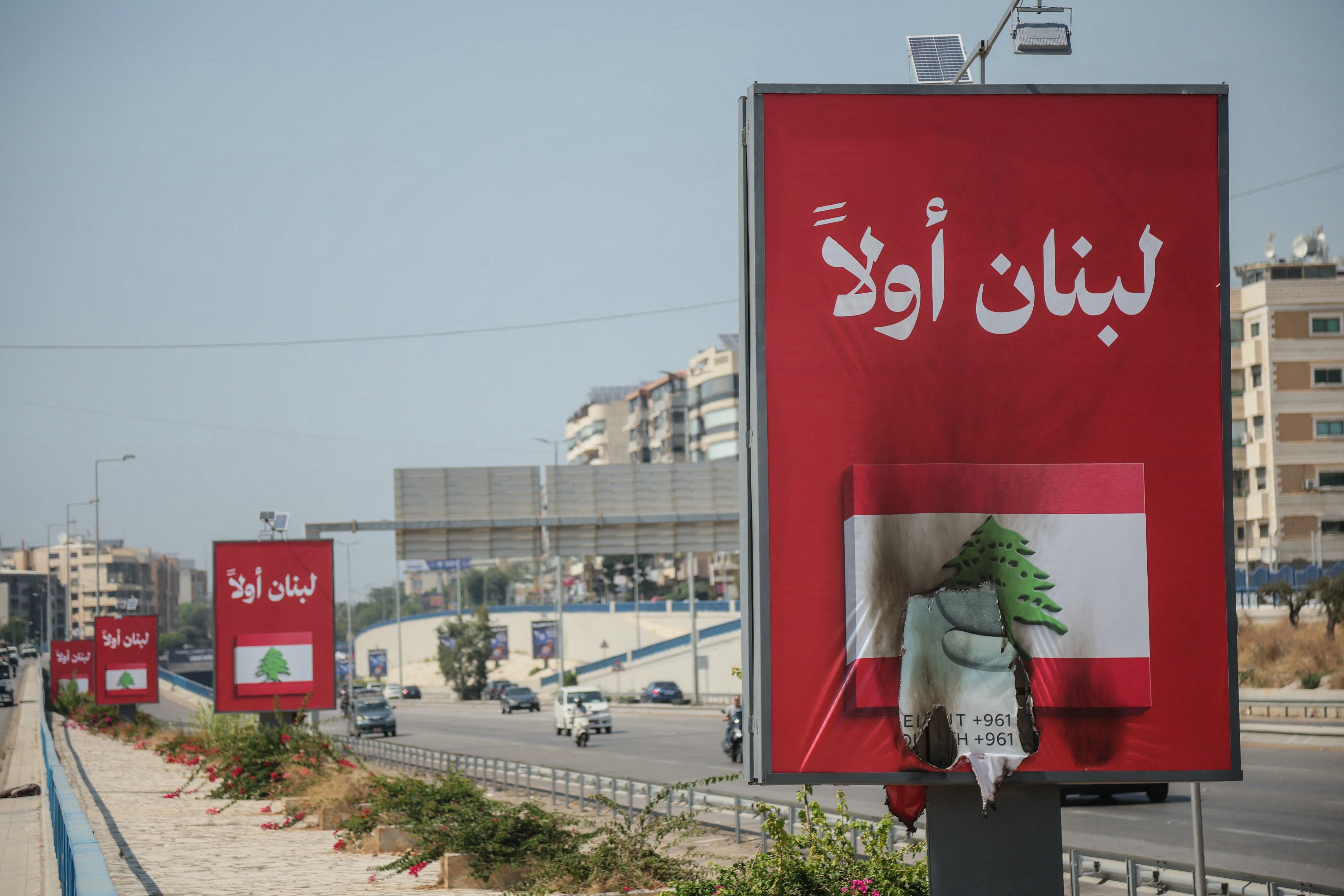 Vehicles drive past billboards that read in Arabic, Lebanon first, one of which has been set on fire along Beirut's airport road near Tehran-backed Hezbollah's stronghold, amidst tensions following Lebanon's framework agreement with Israel on 28 June 2026 (AFP/Getty)