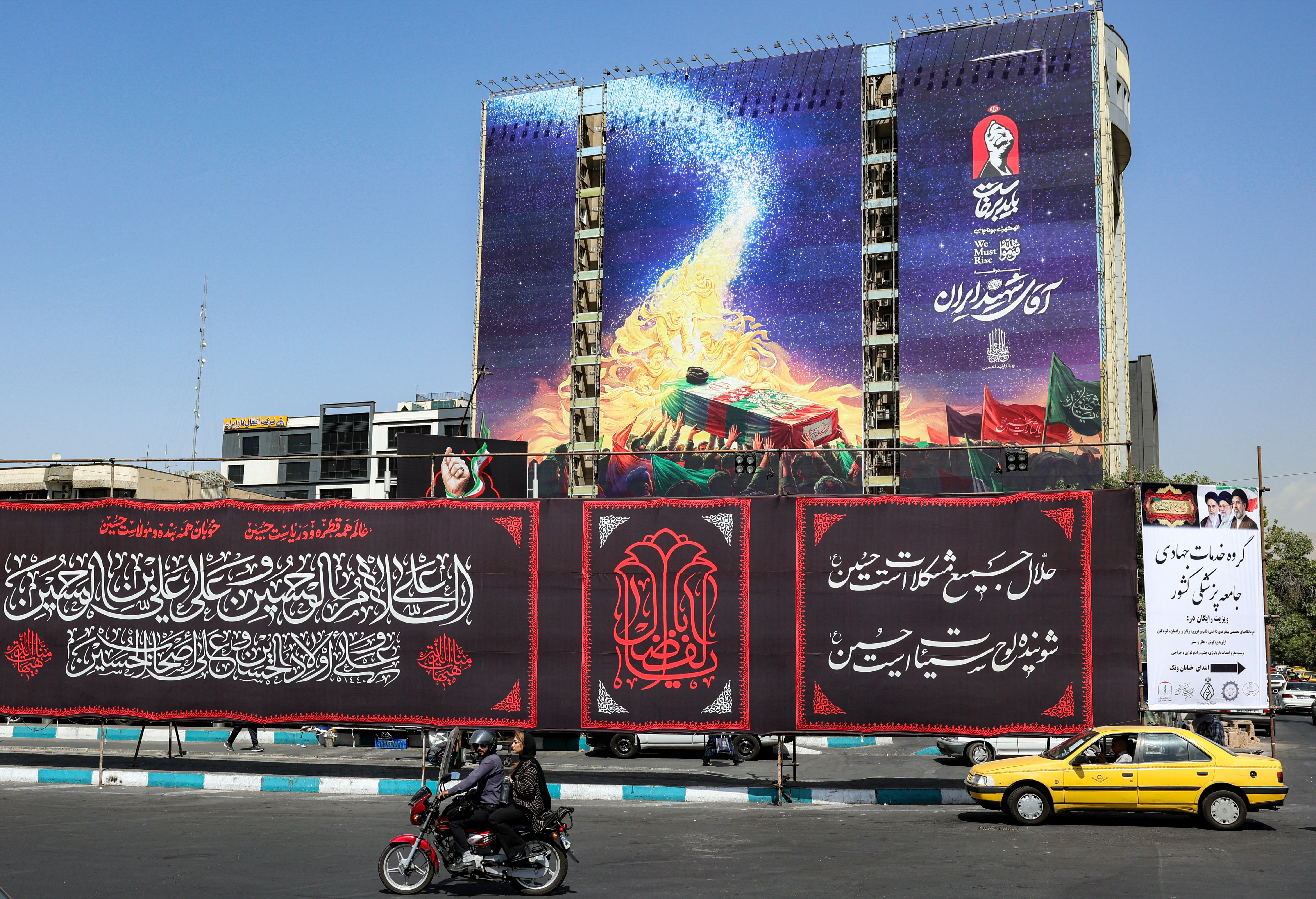Motorists drive vehicles past a mural displayed on the facade of a building depicting late figures aligned with the Iranian government, such as late President Ebrahim Raisi, slain Islamic revolutionary guards commander Qasem Soleimani, slain Lebanese Hezbollah leader Hassan Nasrallah, and others (AFP/Getty)