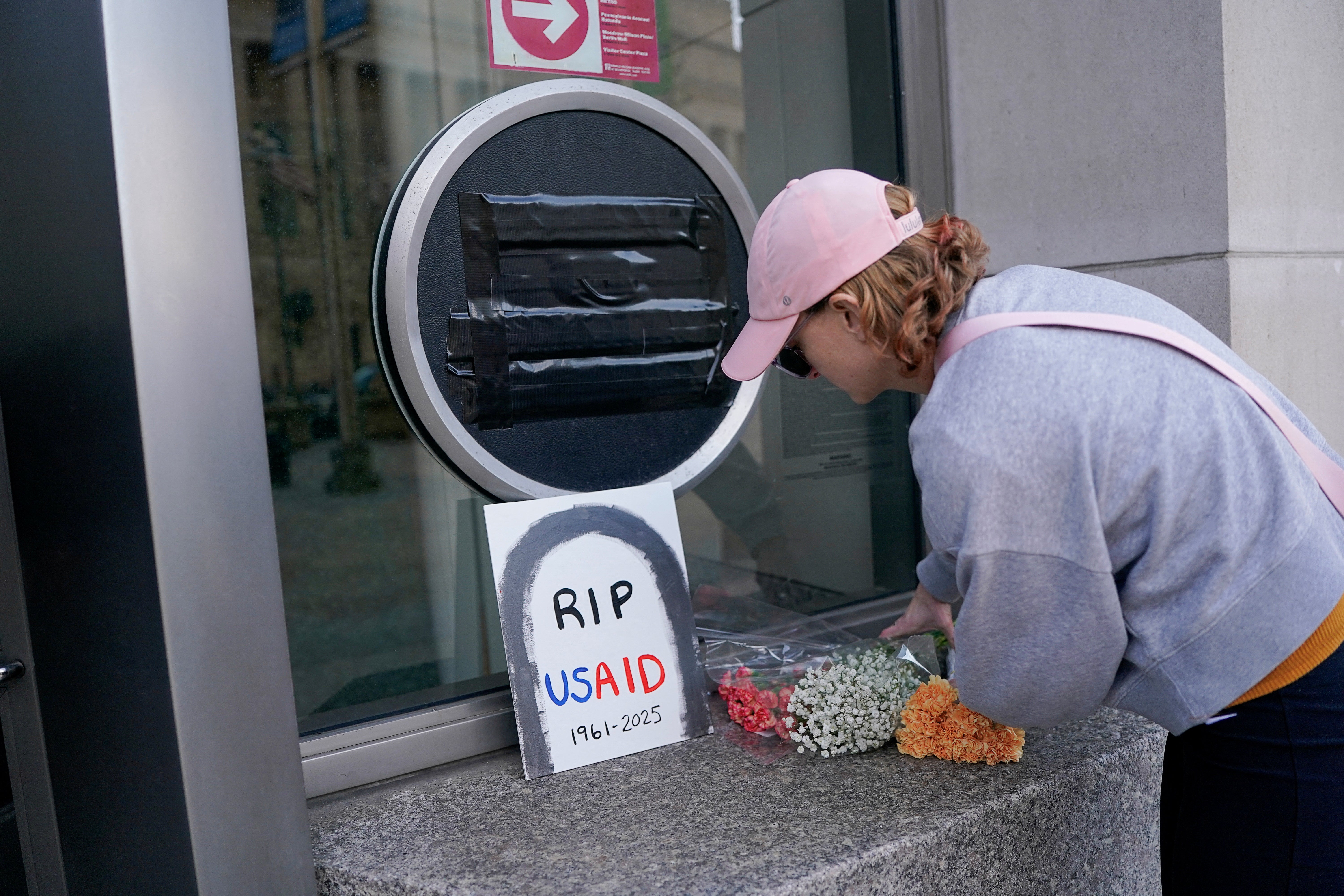 米国ワシントンのUSAID本部で、覆われたUSAIDの看板の横に花を手向ける男性。