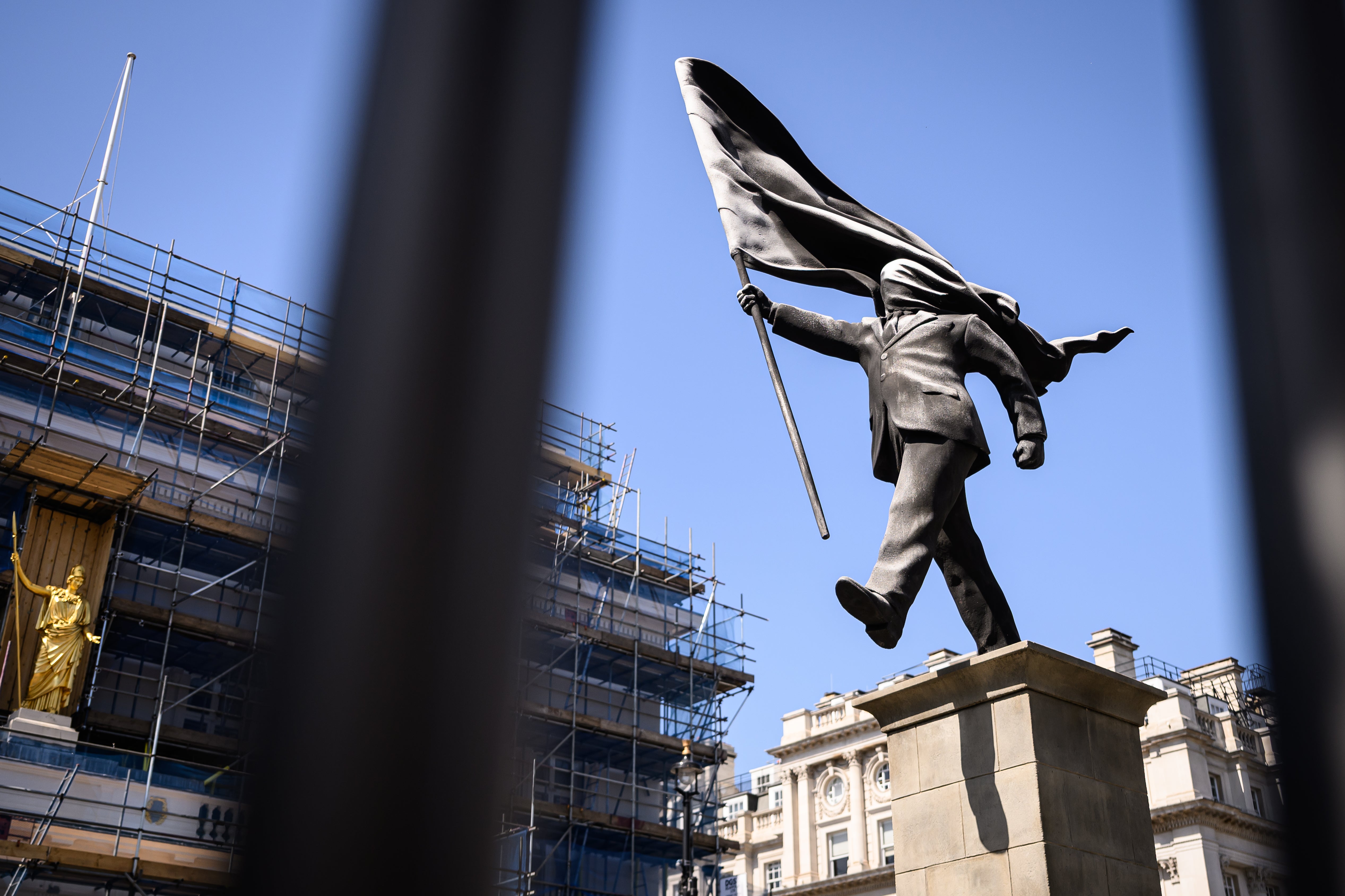 A statue by Banksy depicting a person walking from a plinth, his face covered by a billowing flag, in Waterloo Place in May (Getty)