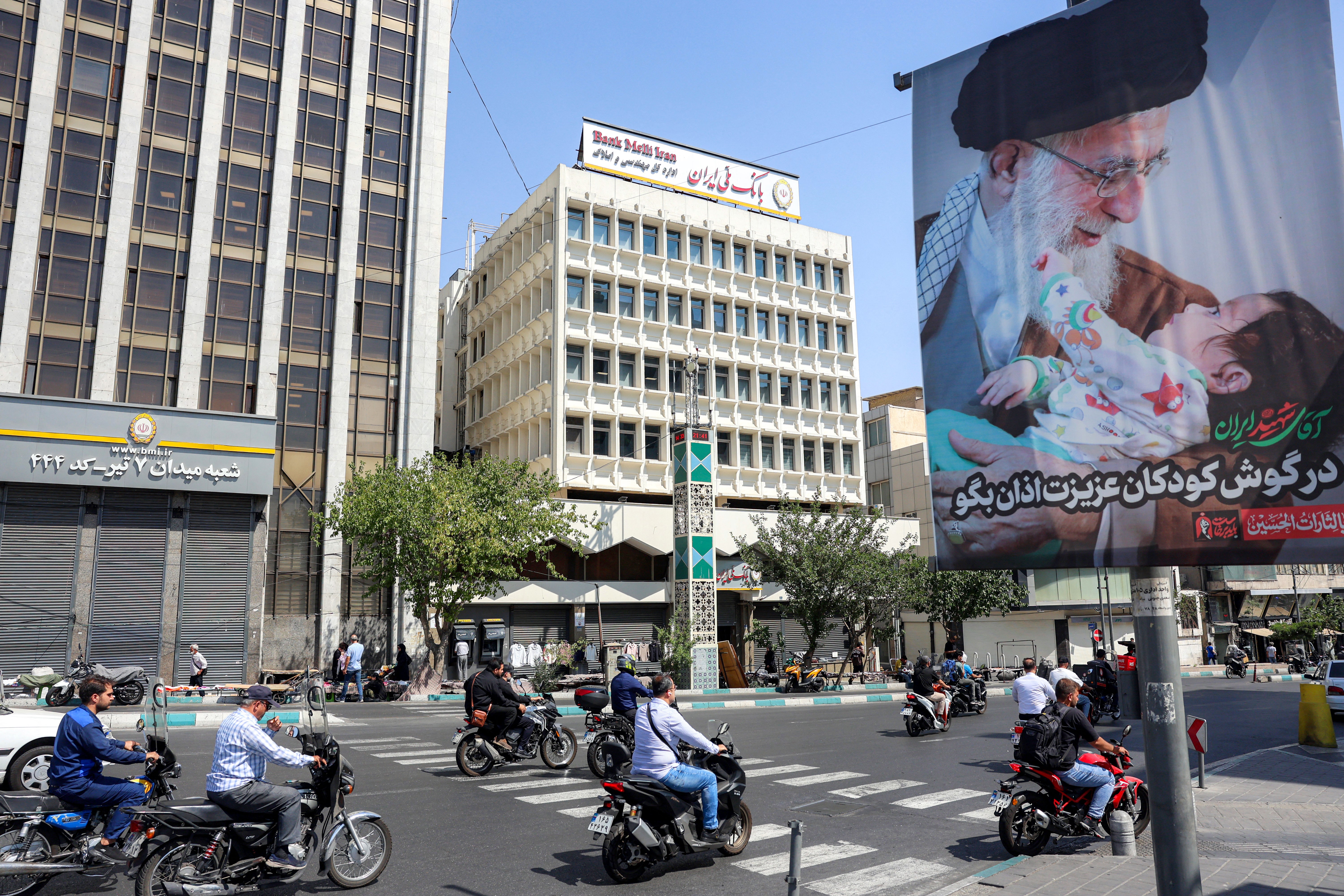 Motorists ride motorcycles along a road past a mourning billboard depicting Iran's slain supreme leader Ali Khamenei, who was killed in a strike on the first day of the US-Israeli wa