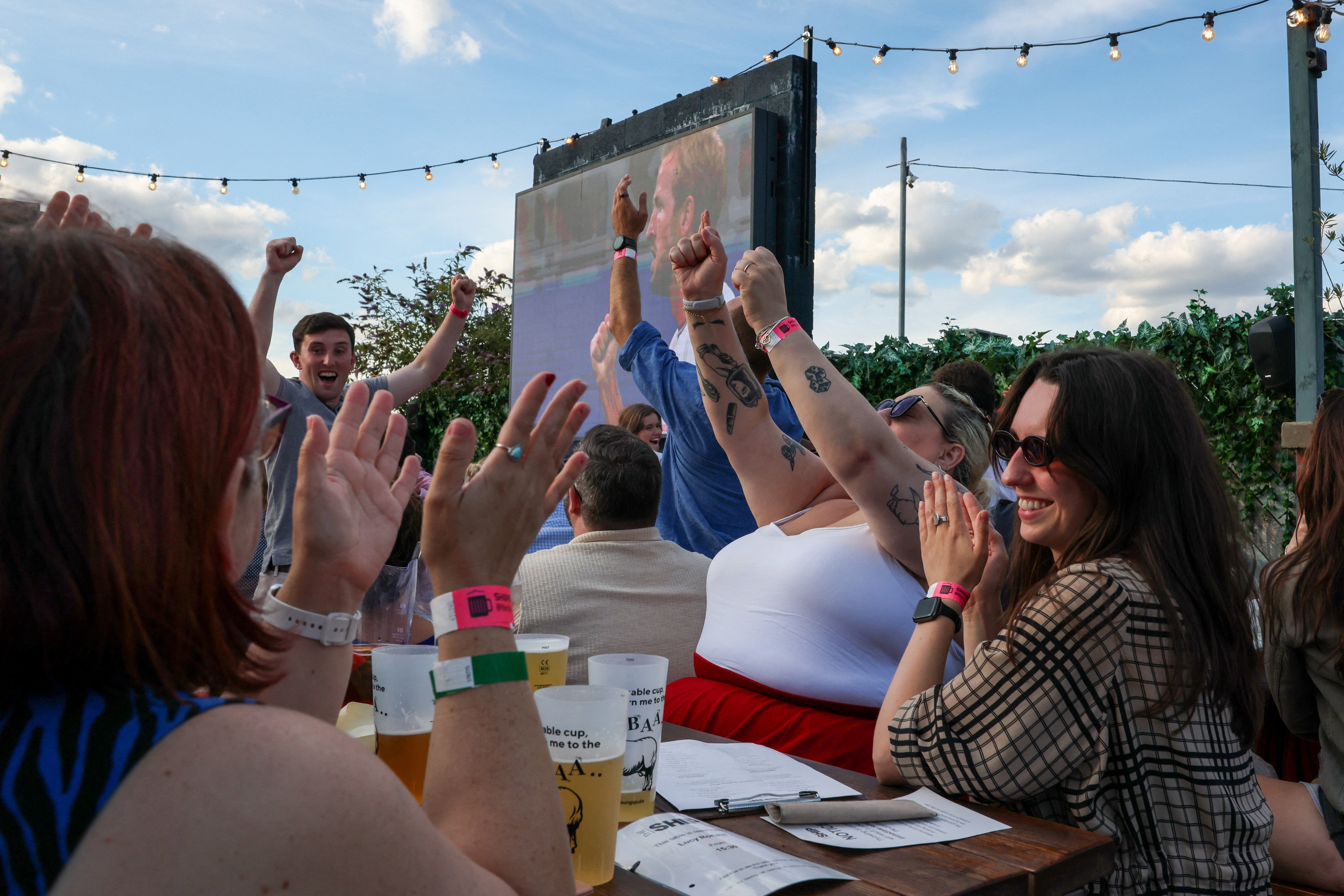 Fans watching the match on a large screen in a pub garden cheer at the final whistle of the England World Cup match against DR Congo in Wandsworth, London