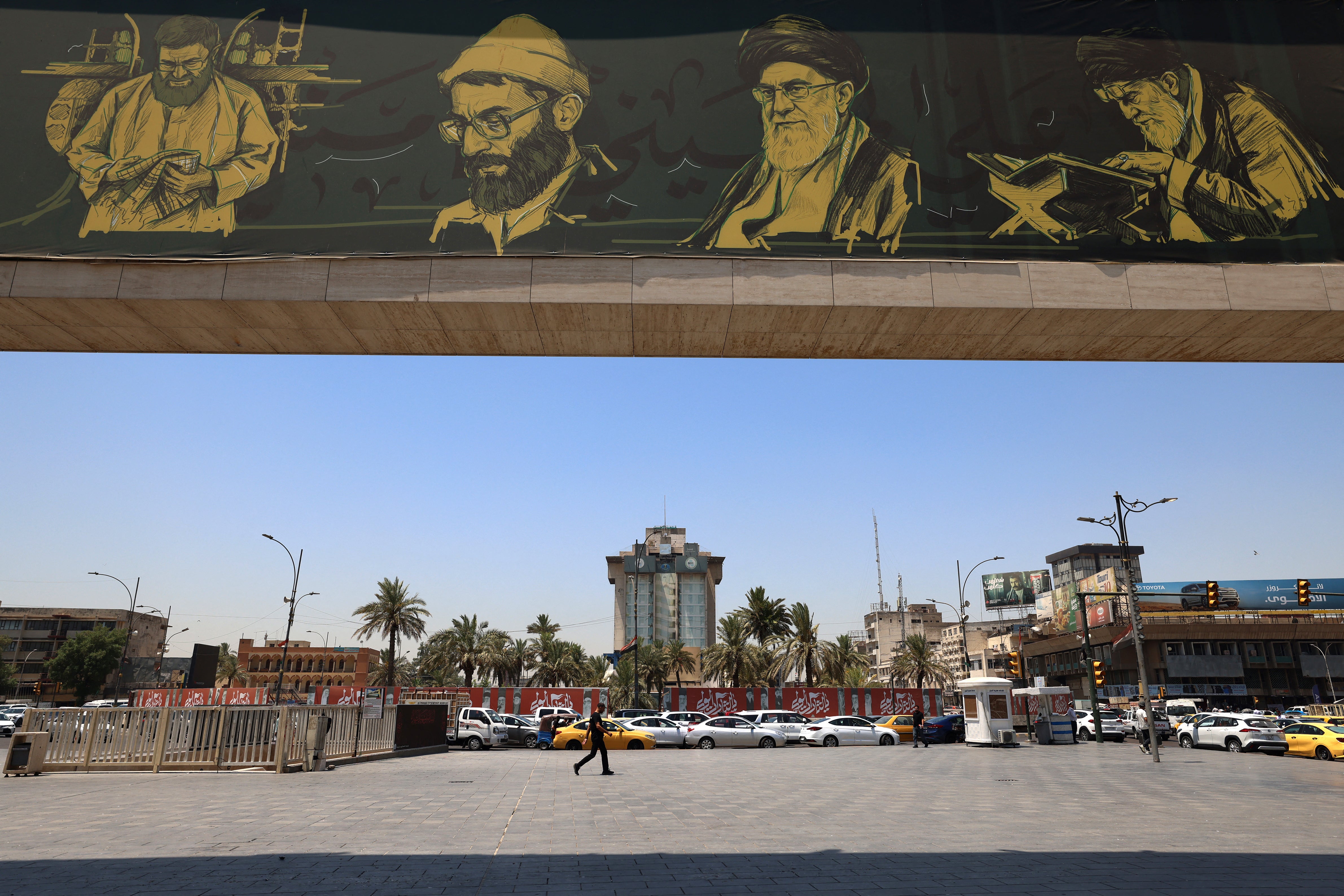 A commuter walks past a billboard bearing pictures of Iran's late supreme leader Ayatollah Ali Khamenei, along a street in Baghdad on July 2, 2026, ahead of his funeral in Tehran. (AFP/Getty)