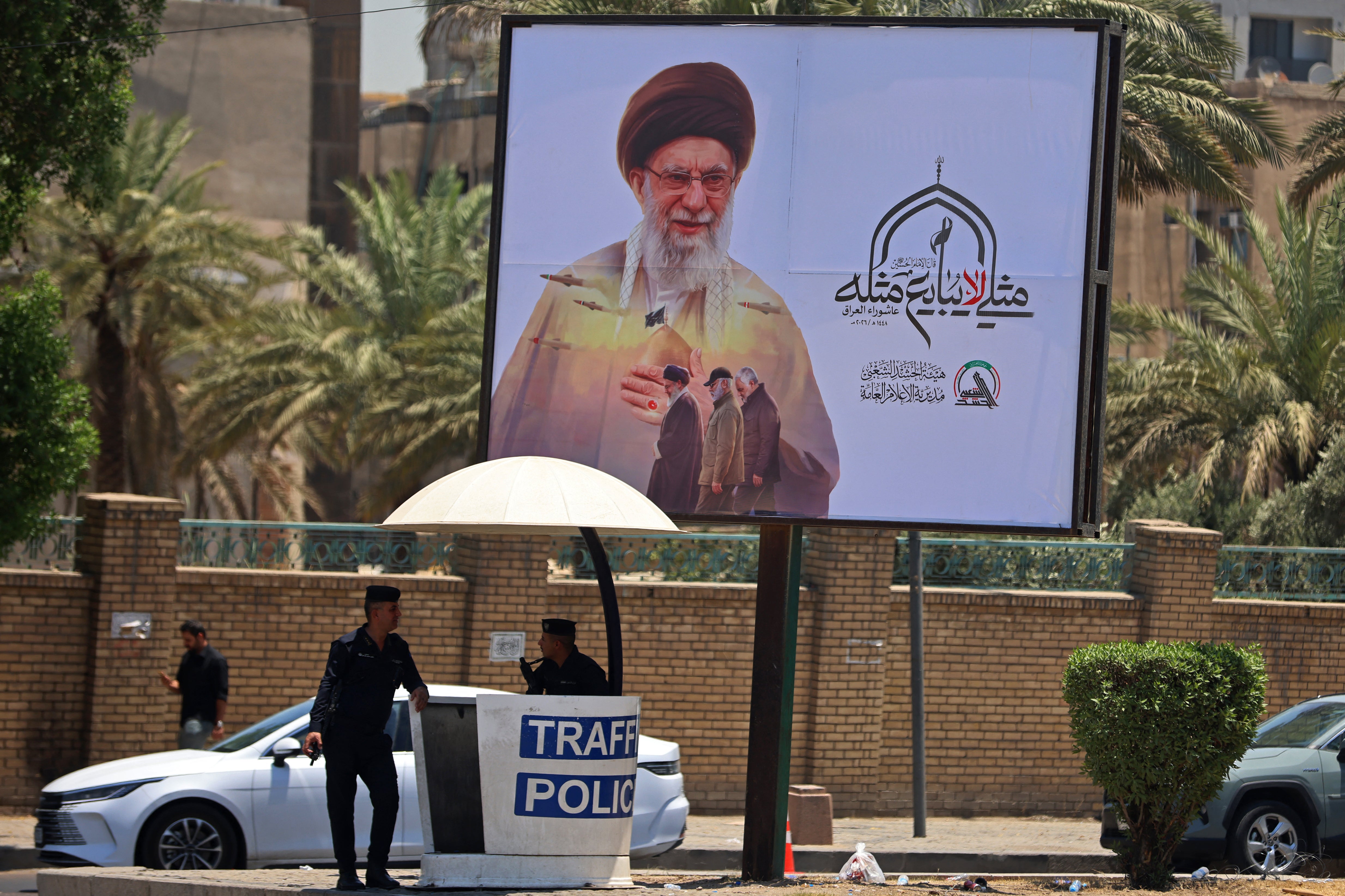 Traffic policemen stand guard under a giant billboard bearing a picture of Iran's late supreme leader Ayatollah Ali Khamenei, along a road junction in Baghdad on July 2, 2026, ahead of his funeral in Tehran. (AFP/Getty)