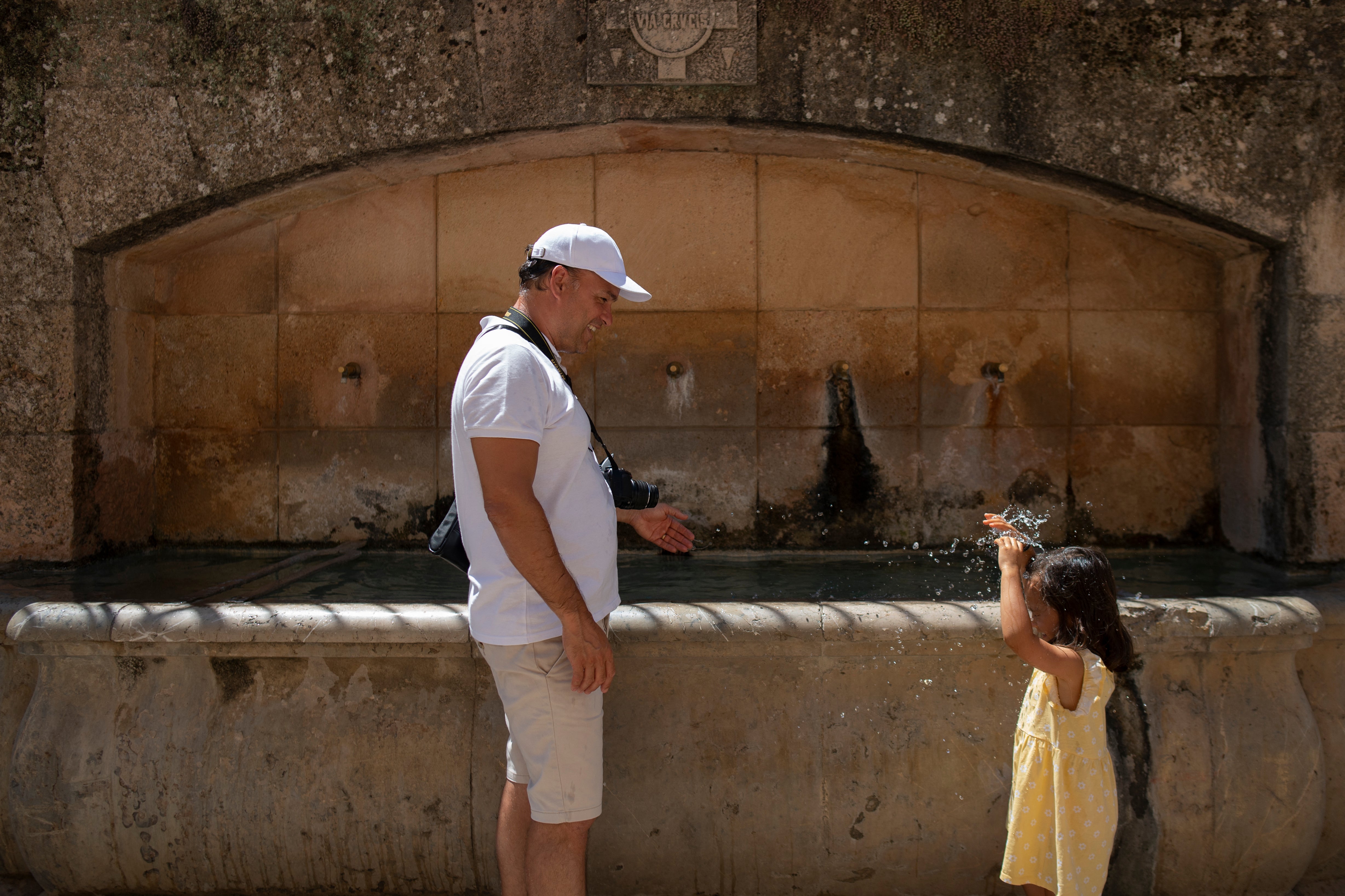 A man cools off with his daughter at a fountain in Ronda, southern Spain. On Reddit threads, Americans rave about living abroad in countries that provide free healthcare, significantly cheaper higher education and access to more affordable everyday needs such as groceries