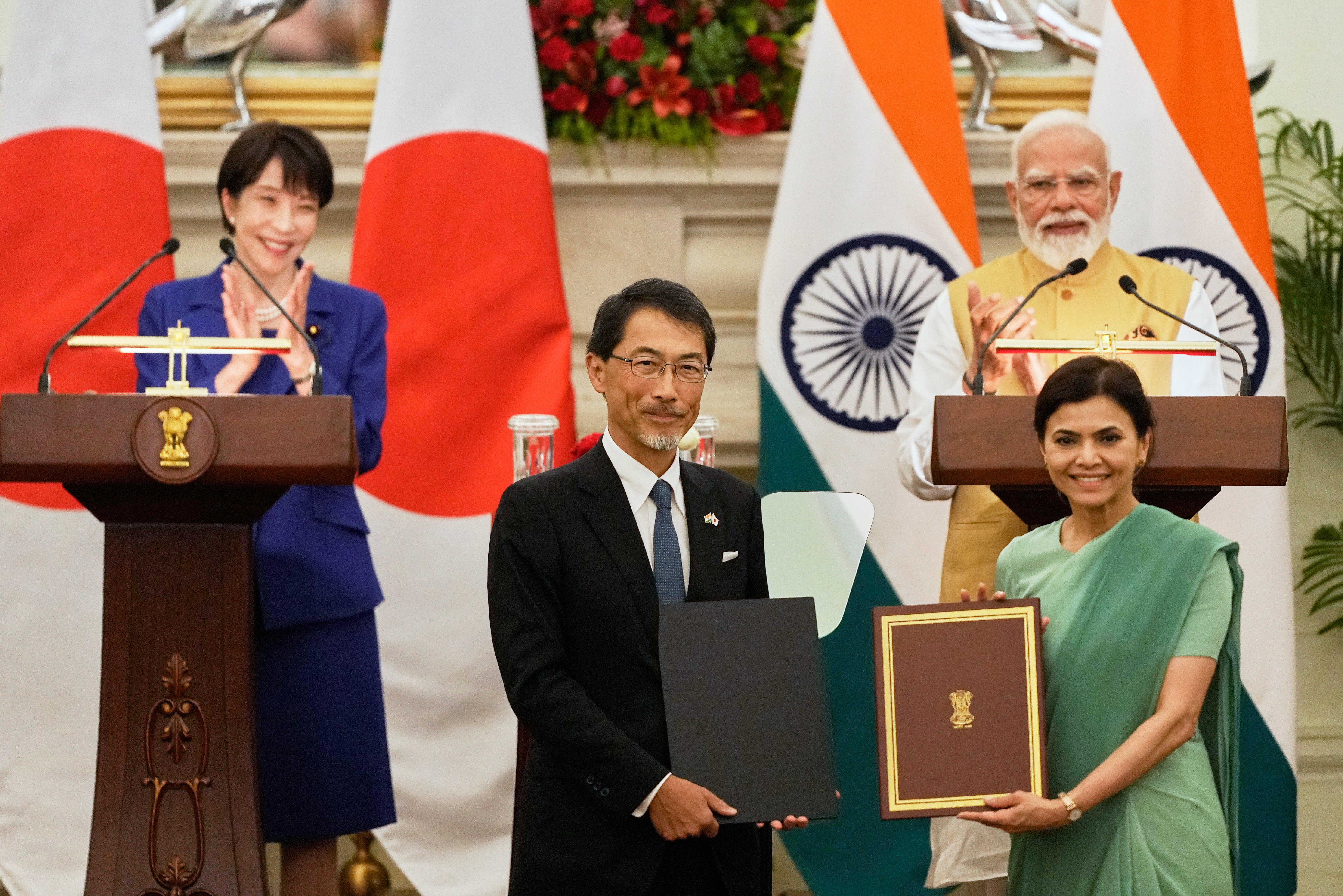 Japan's Prime Minister Sanae Takaichi, left, and India's Prime Minister Narendra Modi, right, applaud as Japan's ambassador to India Ono Keiichi, center left, and India's ambassador to Japan Nagma Mohamed Mallick hold copies of a signed bilateral agreement after their delegation level meeting in New Delhi, India