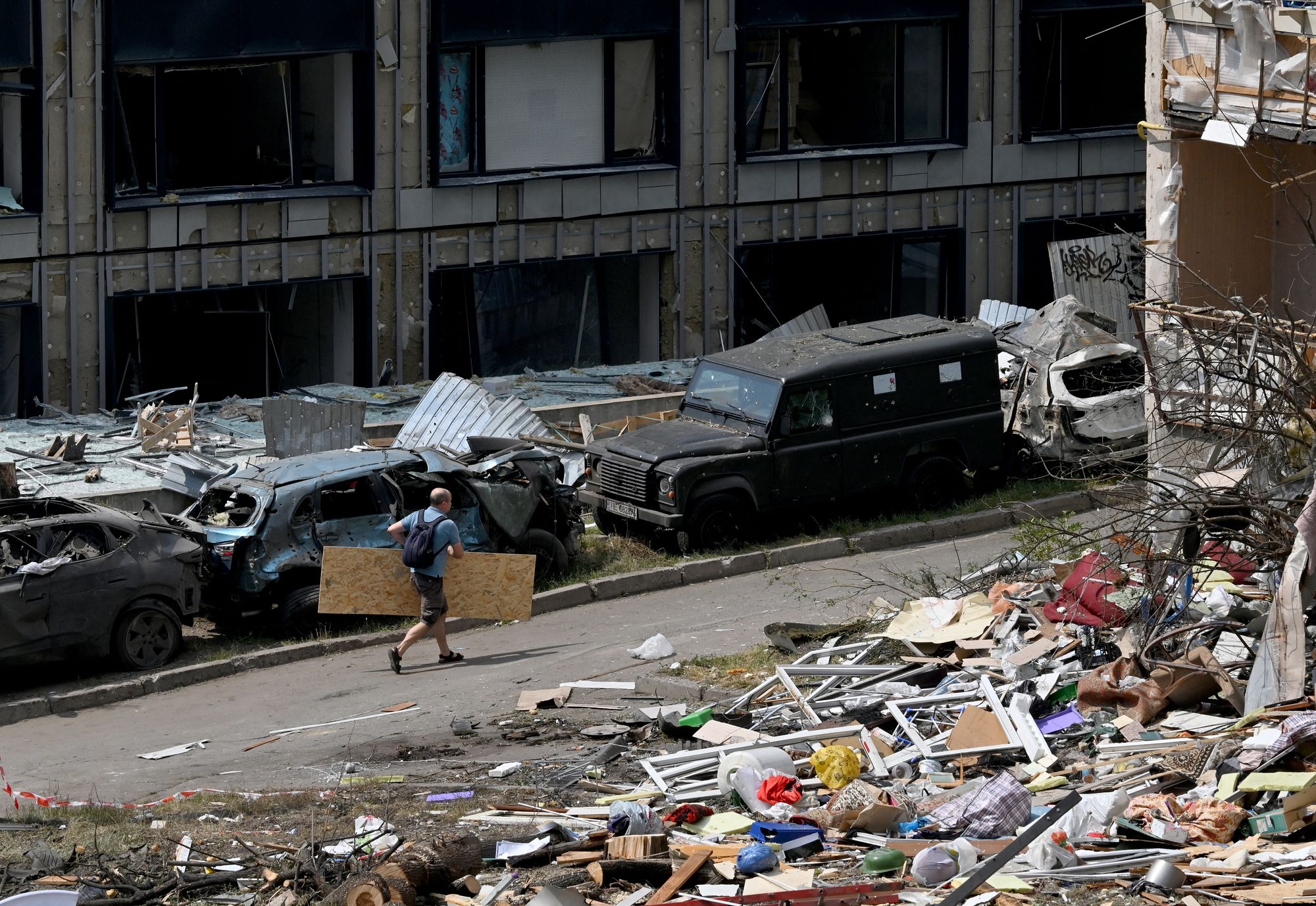 A local resident carries a plywood board past debris and a residential building damaged following a Russian air attack on Kyiv