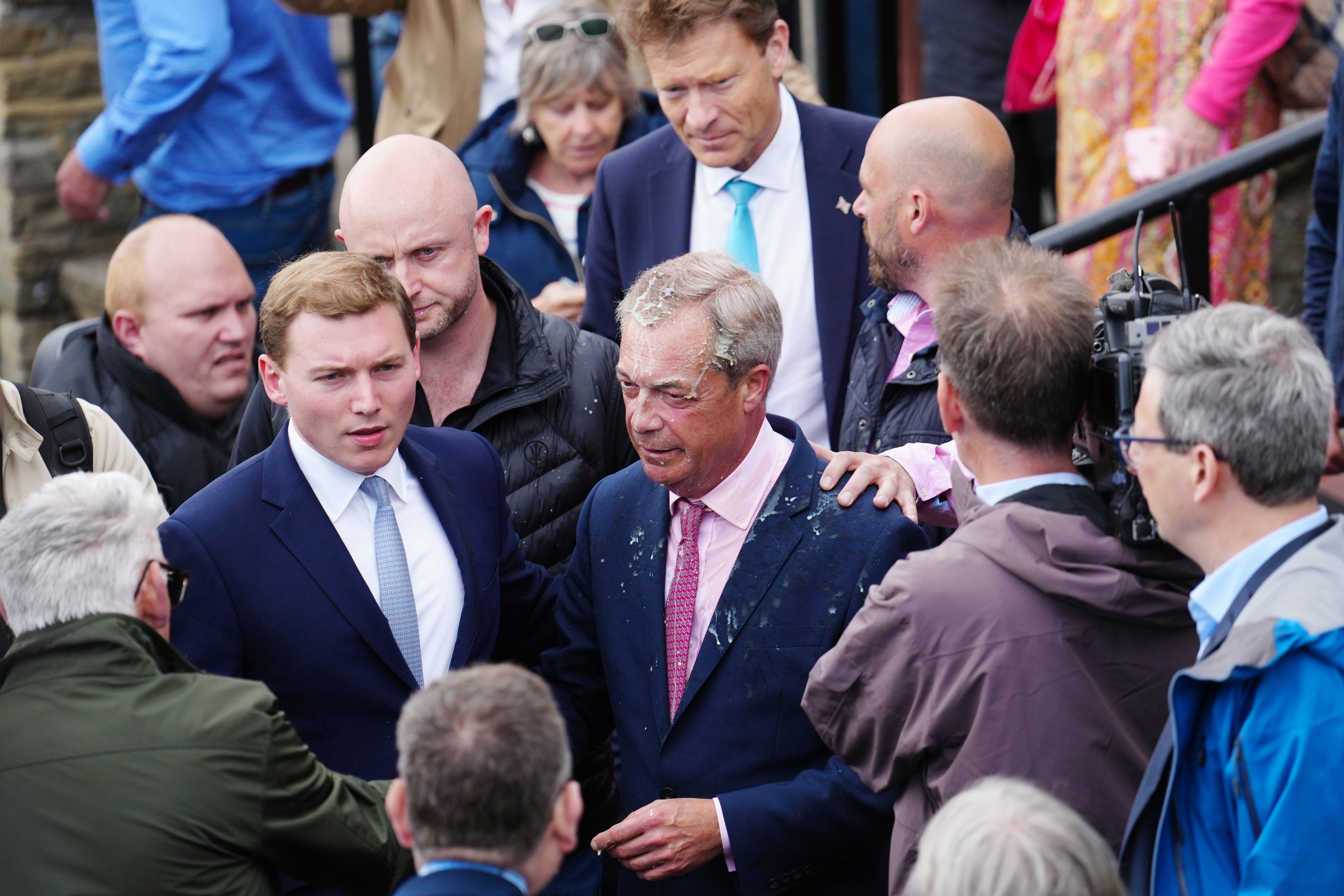 George Cottrell (L) looks on as Reform UK party leader Nigel Farage reacts after a woman threw a drink over him, as he launches his election candidacy at Clacton Pier on June 4, 2024 in Clacton-on-Sea, England.