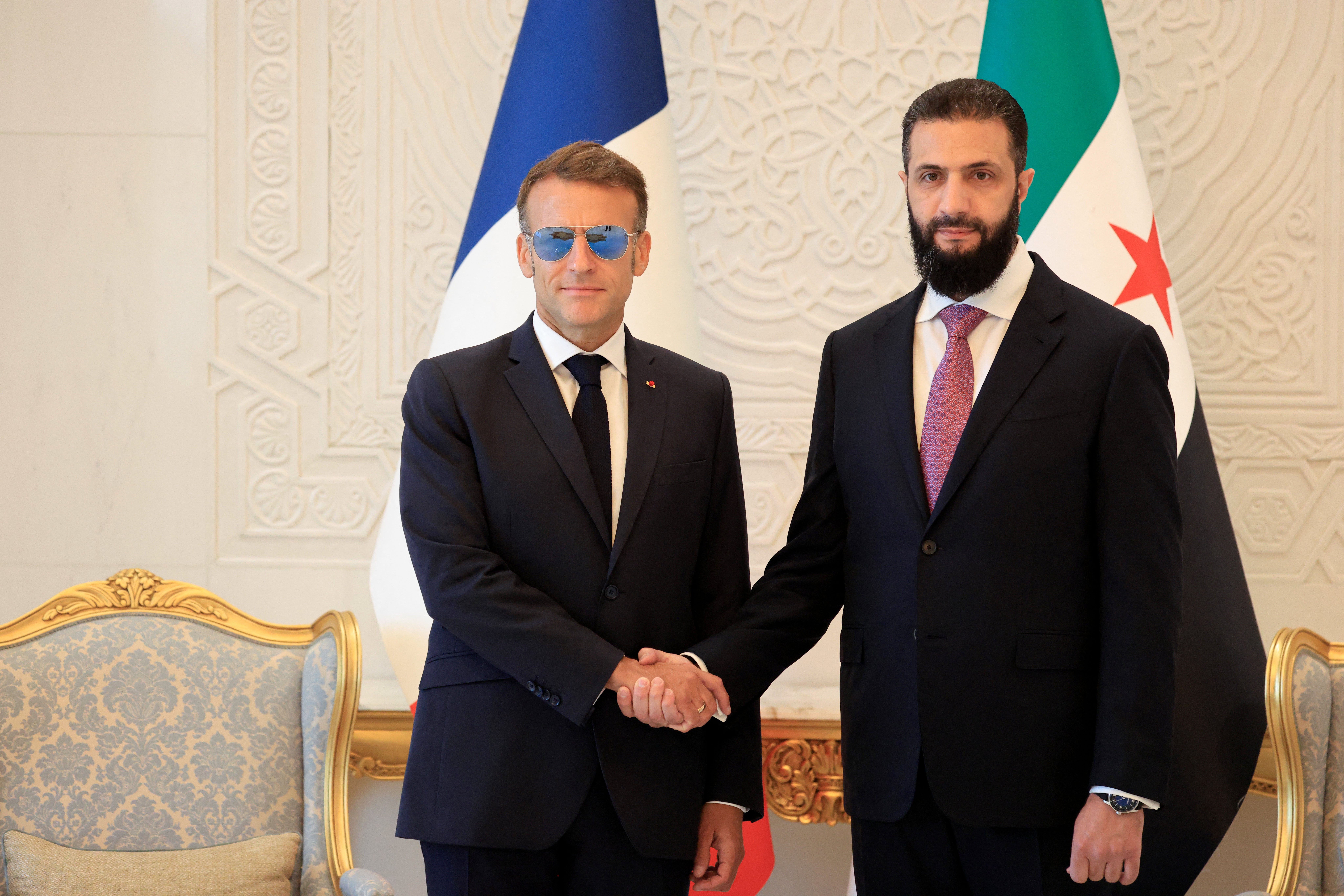 France's President Emmanuel Macron (L) shakes hands with Syrian President Ahmed al-Sharaa ahead of their meeting at the People's Palace in Damascus