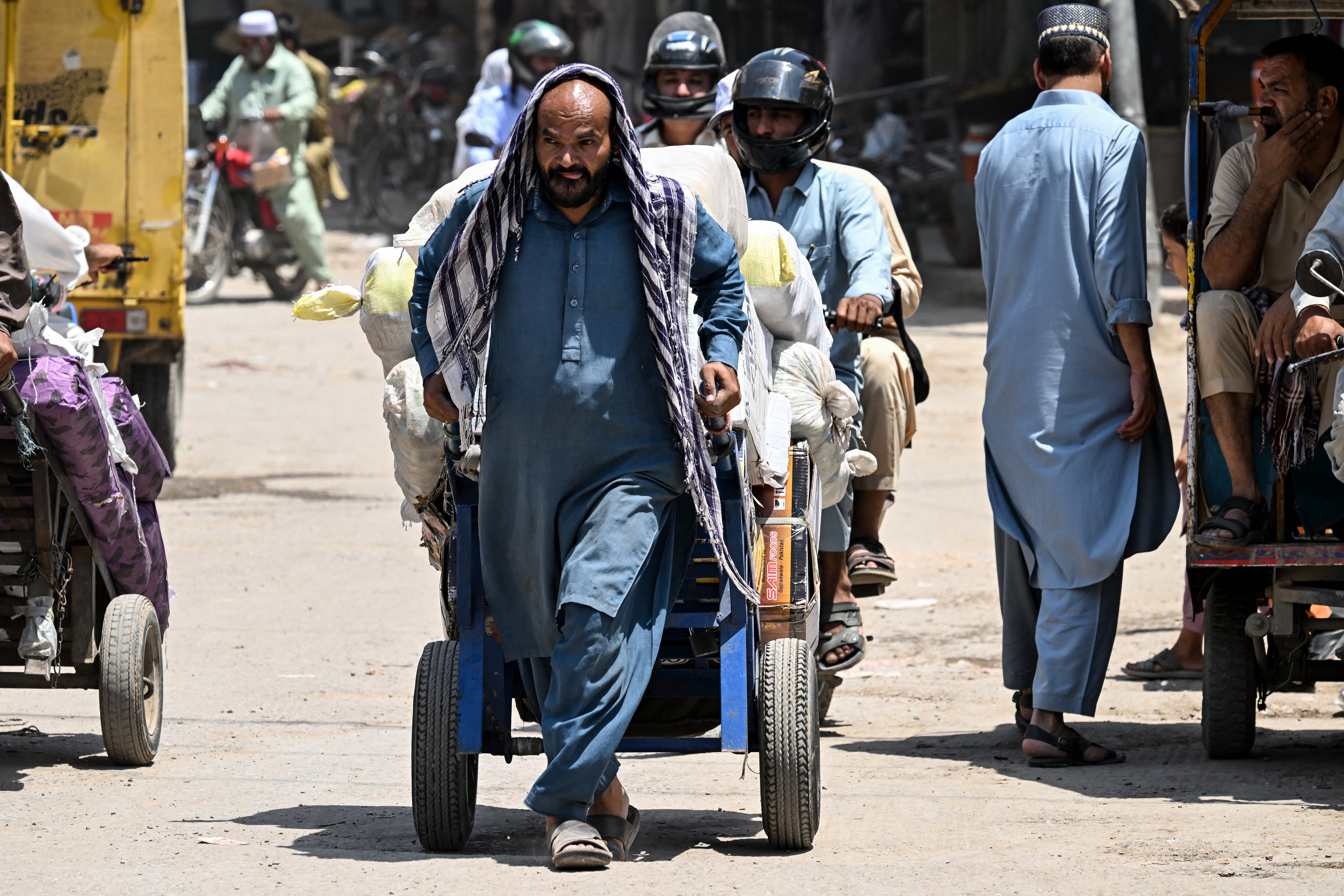 A labourer shields his head with a cloth as he hauls a loaded cart amid a heatwave in Rawalpindi, Pakistan