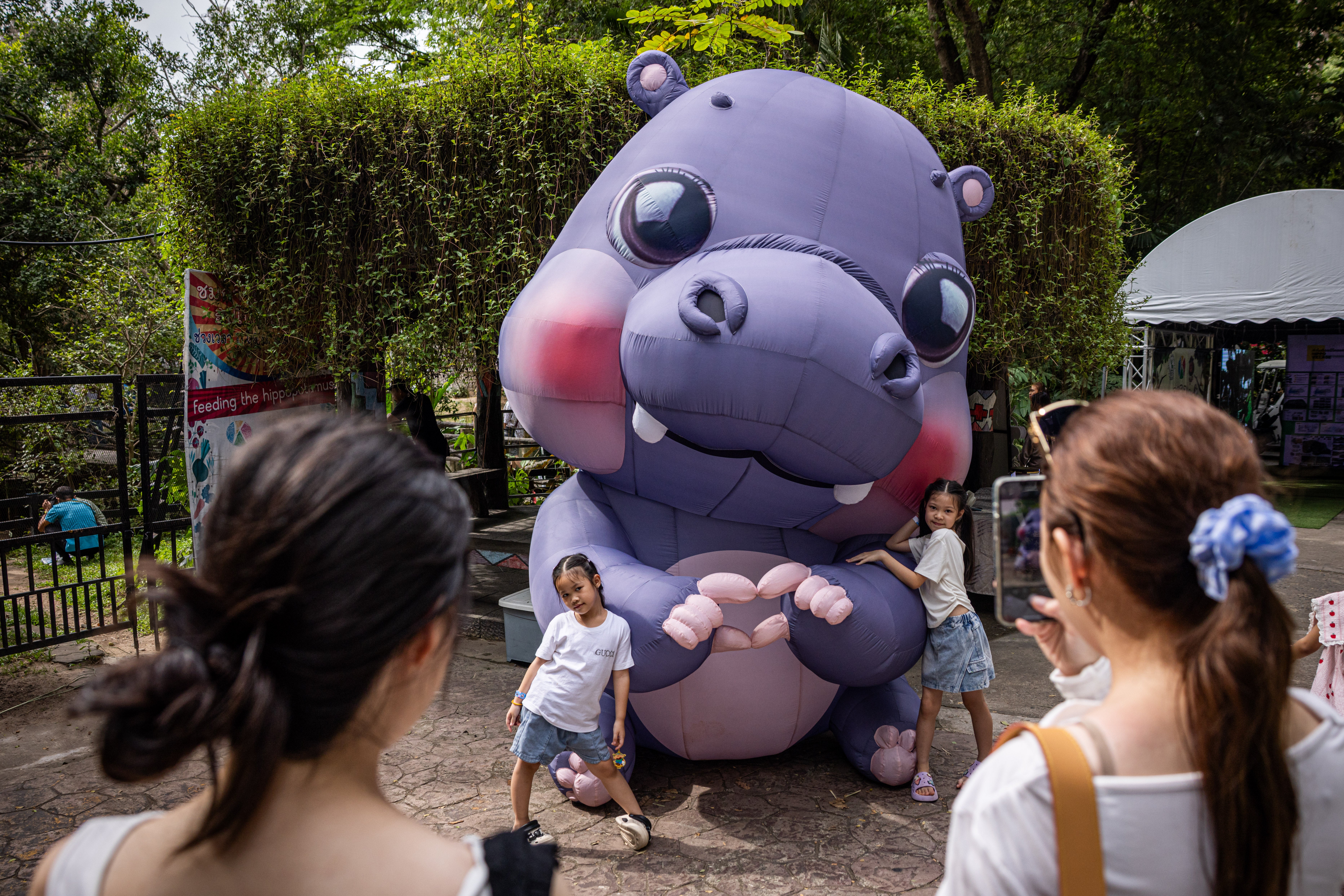 Children pose for pictures with a giant Moo Deng during a celebration of her first birthday at the Khao Kheow Open Zoo