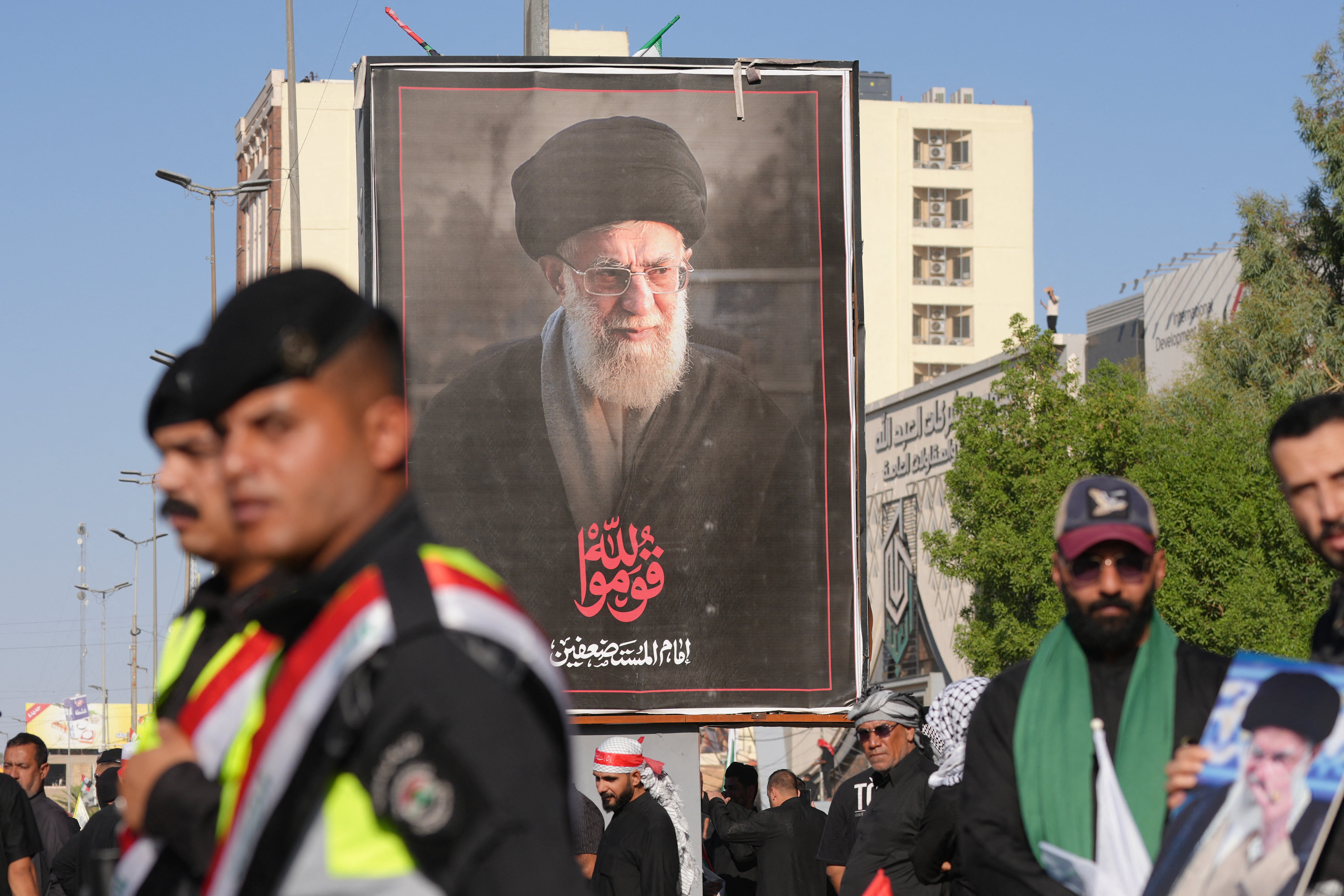 Security forces stand guard in front of a portrait of Iran's slain supreme leader Ali Khamenei as mourners gather for a funeral procession in Najaf on July 8, 2026