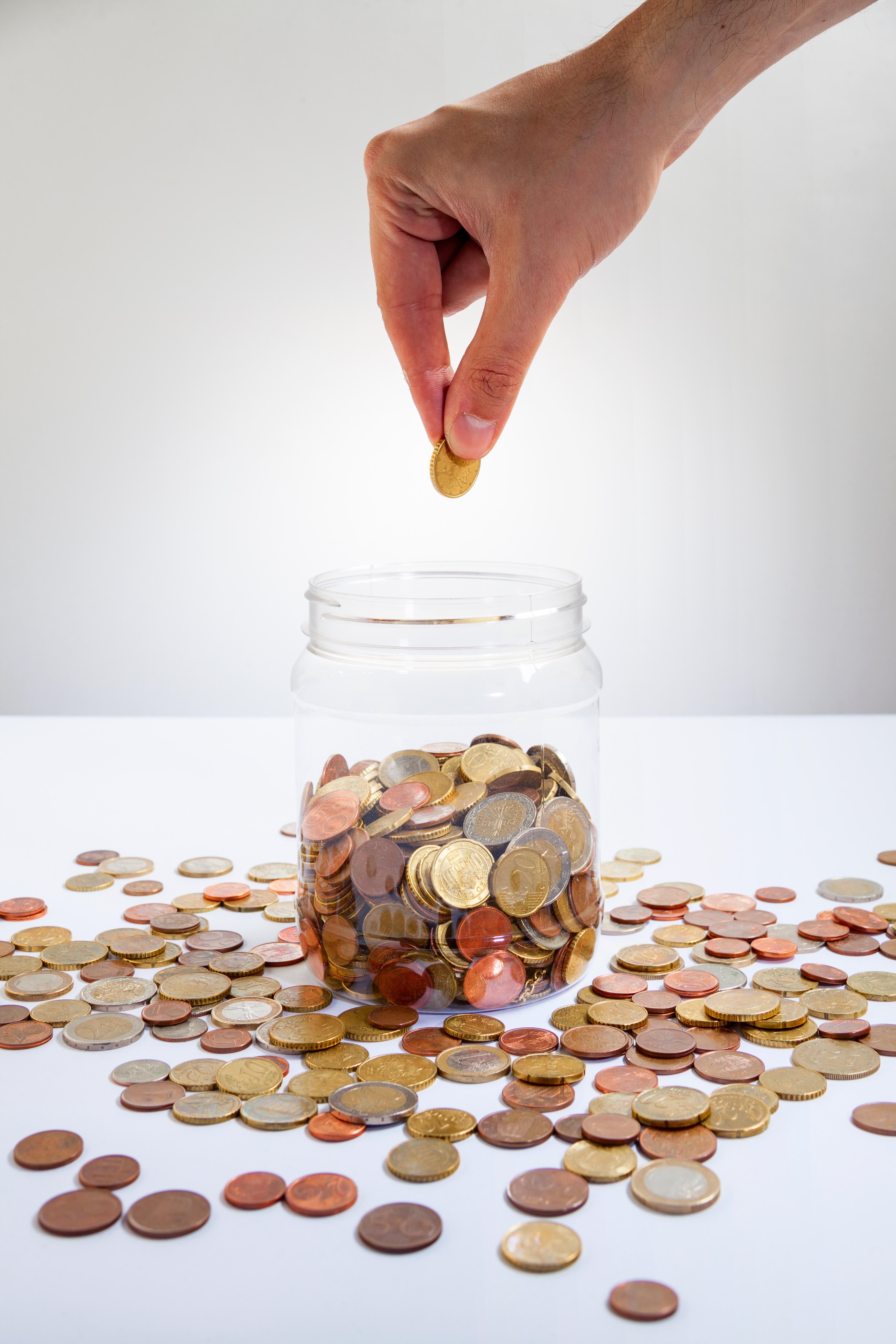 Hand putting coins into a glass jar (Alamy/PA)