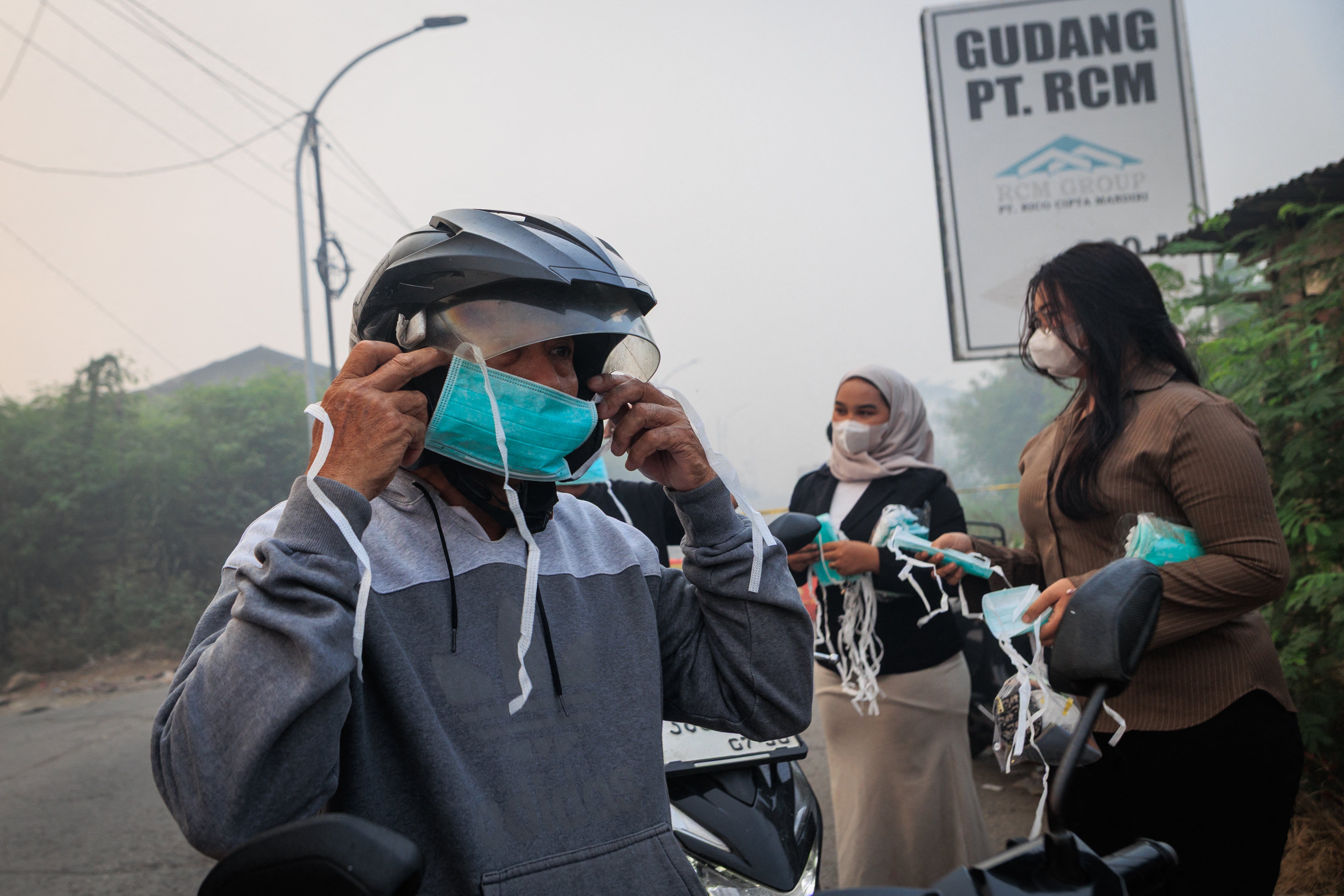 A man wears a face mask distributed by volunteers as smoke billows from a fire at the Jatiwaringin landfill (AFP/Getty)