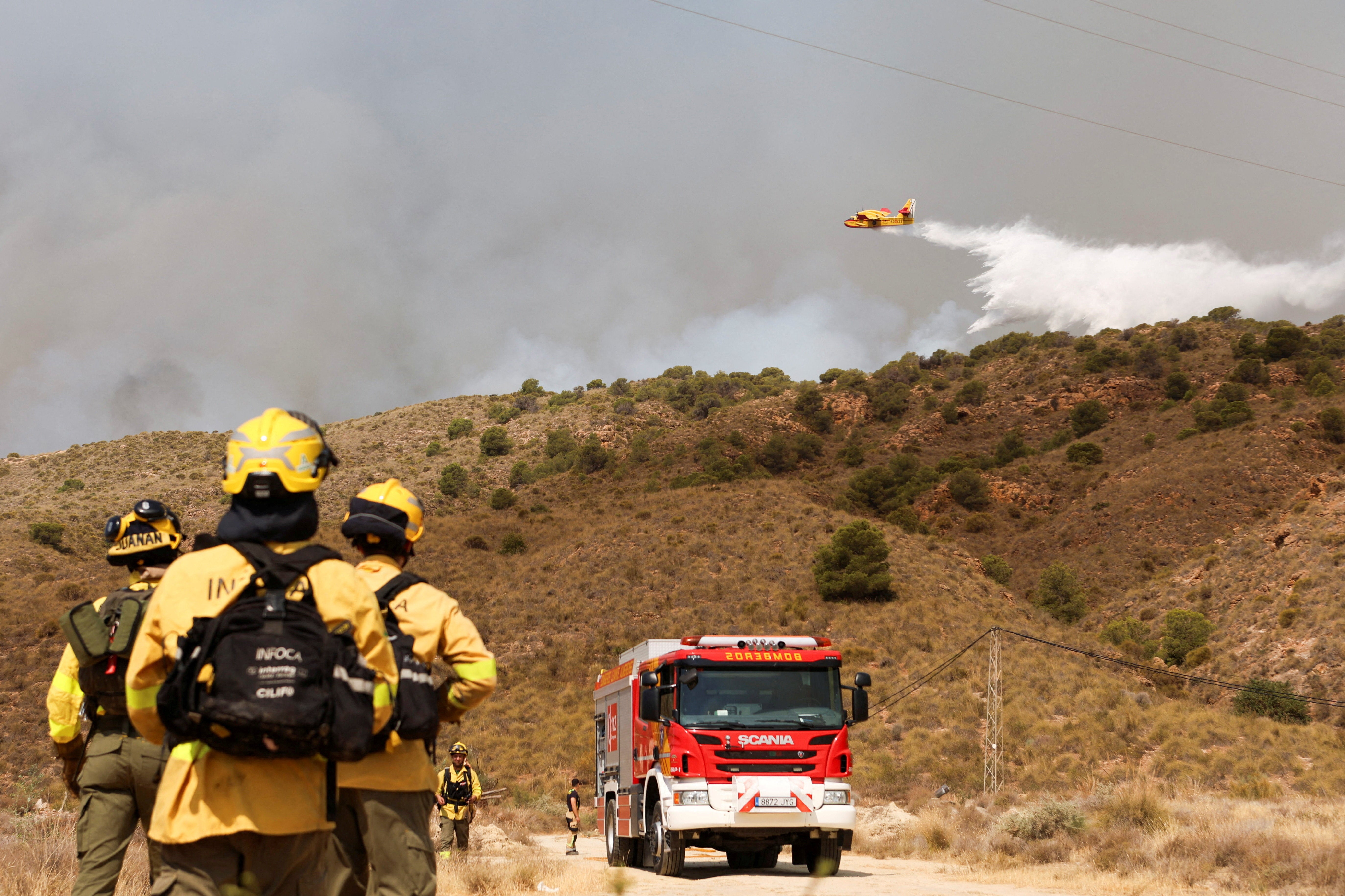 Forest firefighters look on as a firefighting plane dumps water during a wildfire in Los Gallardos, Almeria, Spain