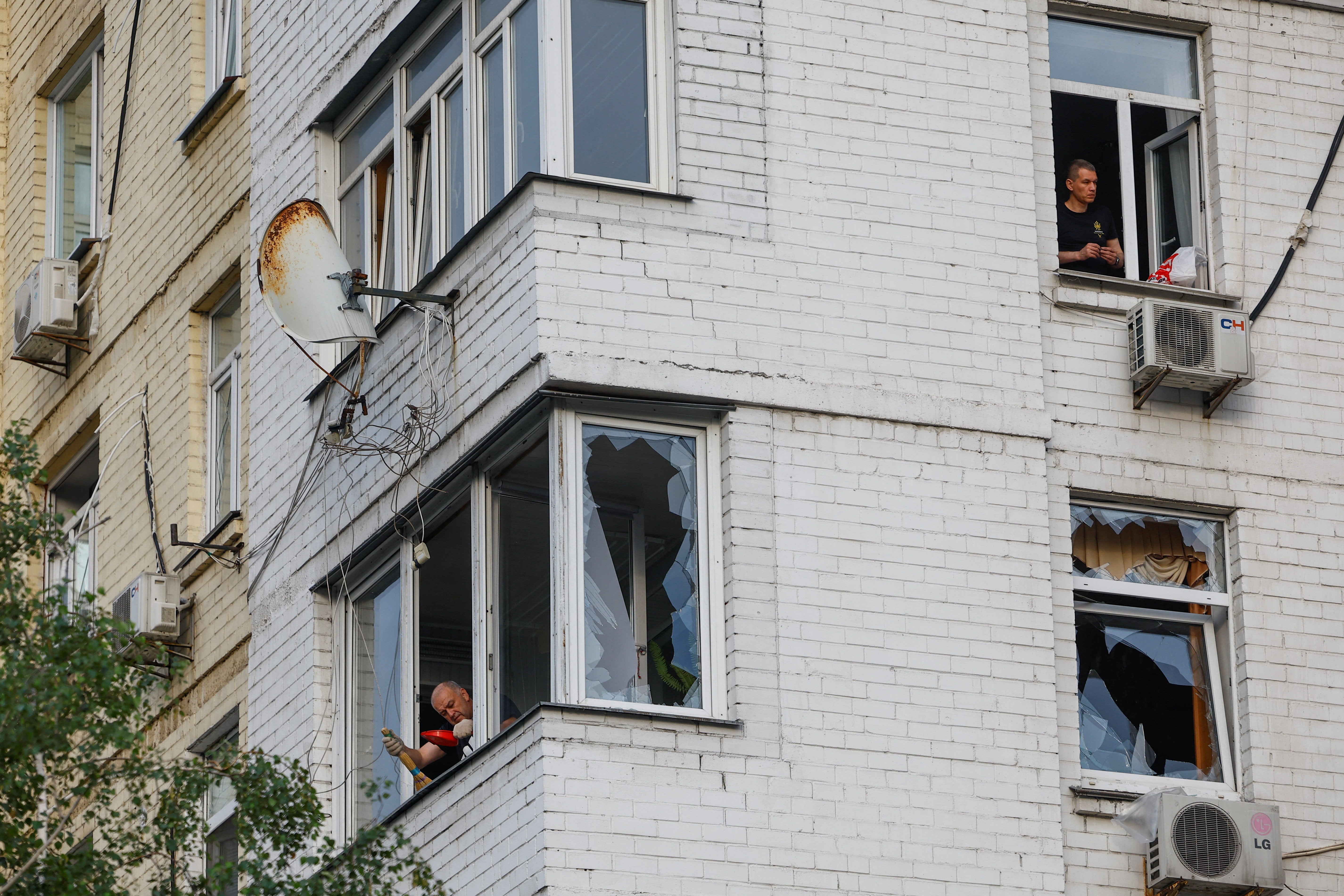 Residents remove pieces of glass from broken windows of their apartments, which were damaged during Russian missile strikes on Kyiv