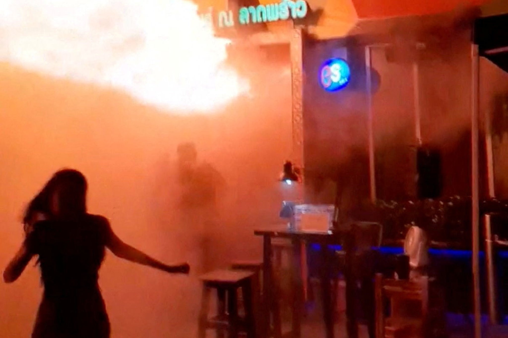 A person runs as flames rise at a bar in Bangkok, Thailand.