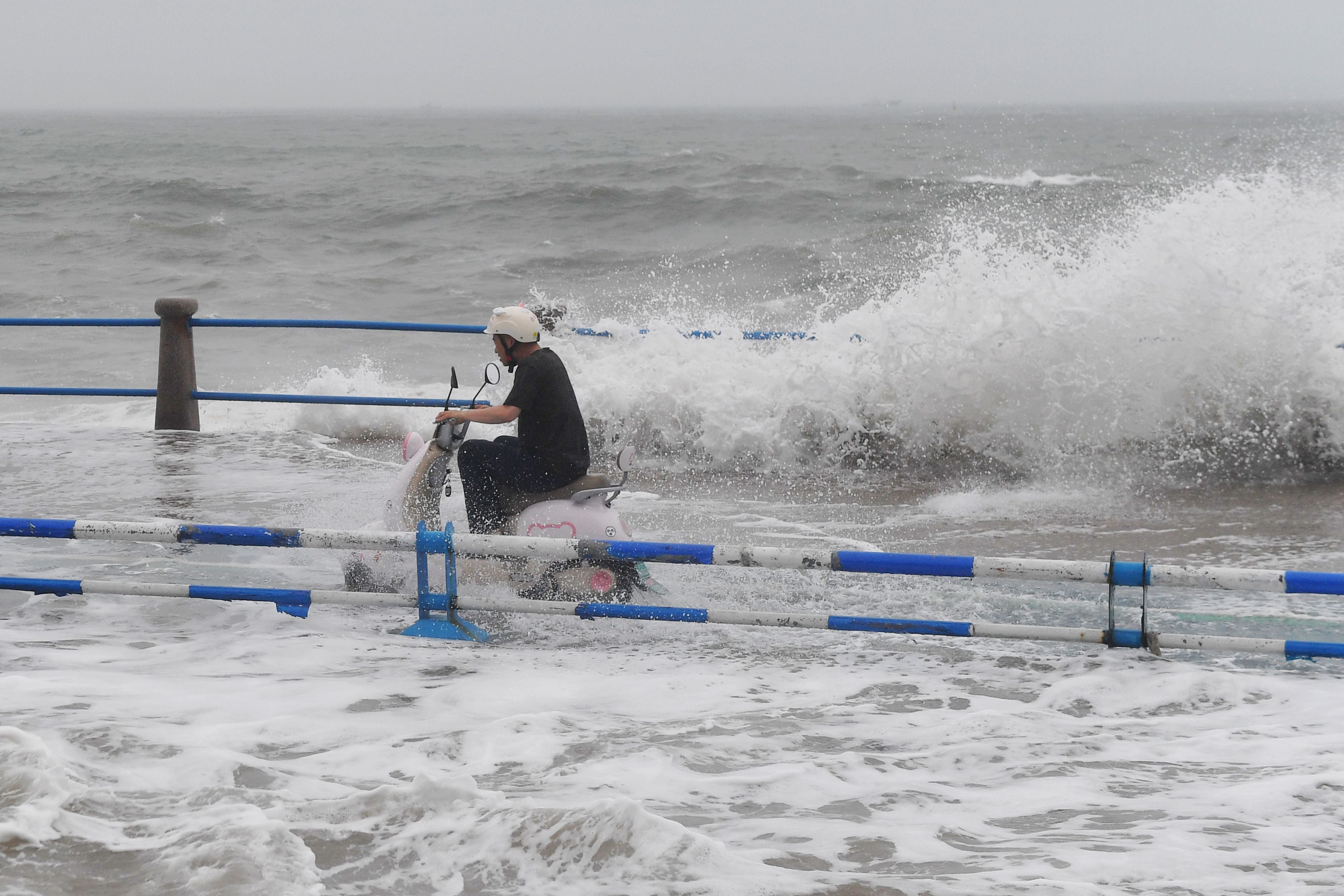 A motorist tries to ride past waves crashing on the shore ahead of Typhoon Bavi in Qingdao in eastern China's Shandong province, Sunday (AP)