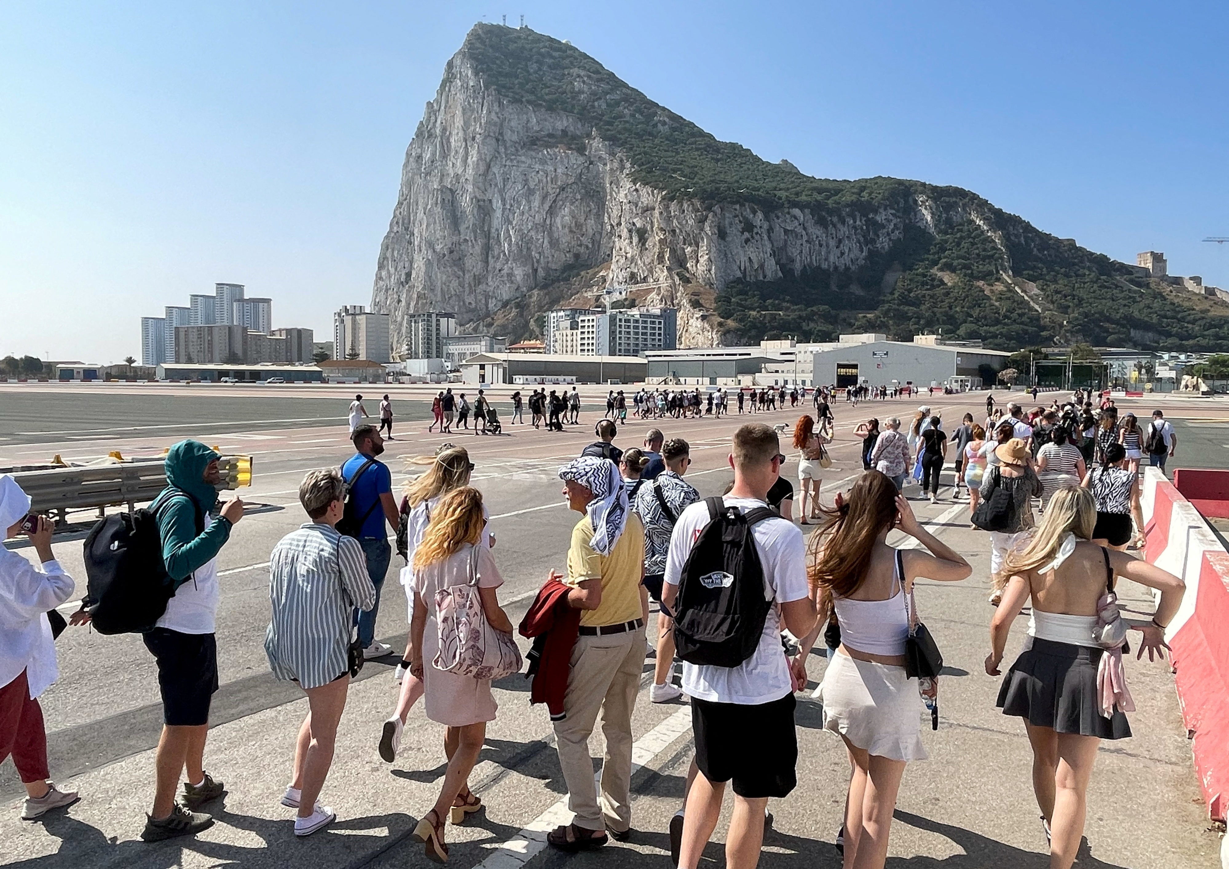 Tourists cross the tarmac of the airport in front of the Rock