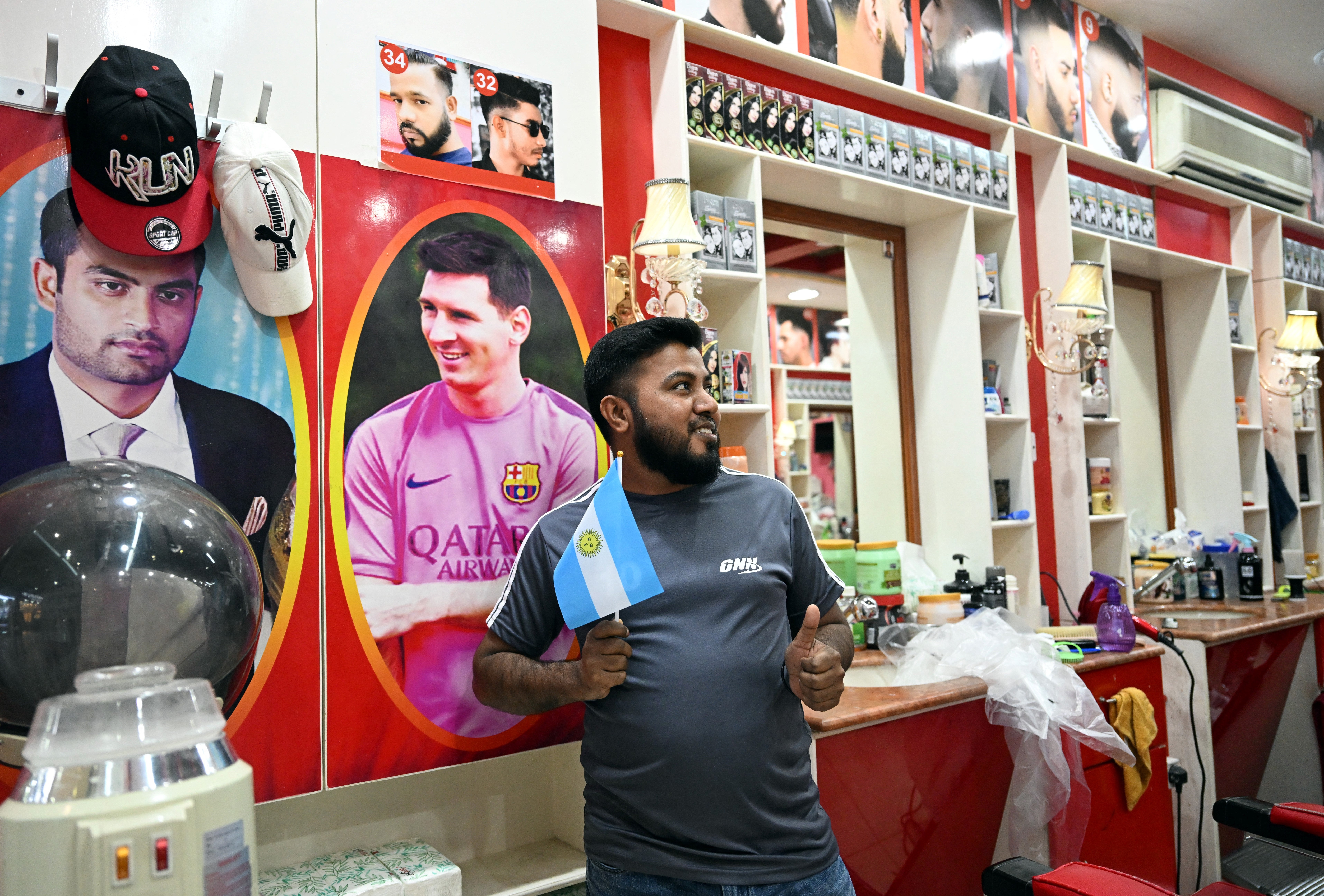 File. A worker of Bangladesh poses with an Argentinian flag in front a photo of Argentina's forward Lionel Messi in a hairdresser shop in Doha on December 6, 2022