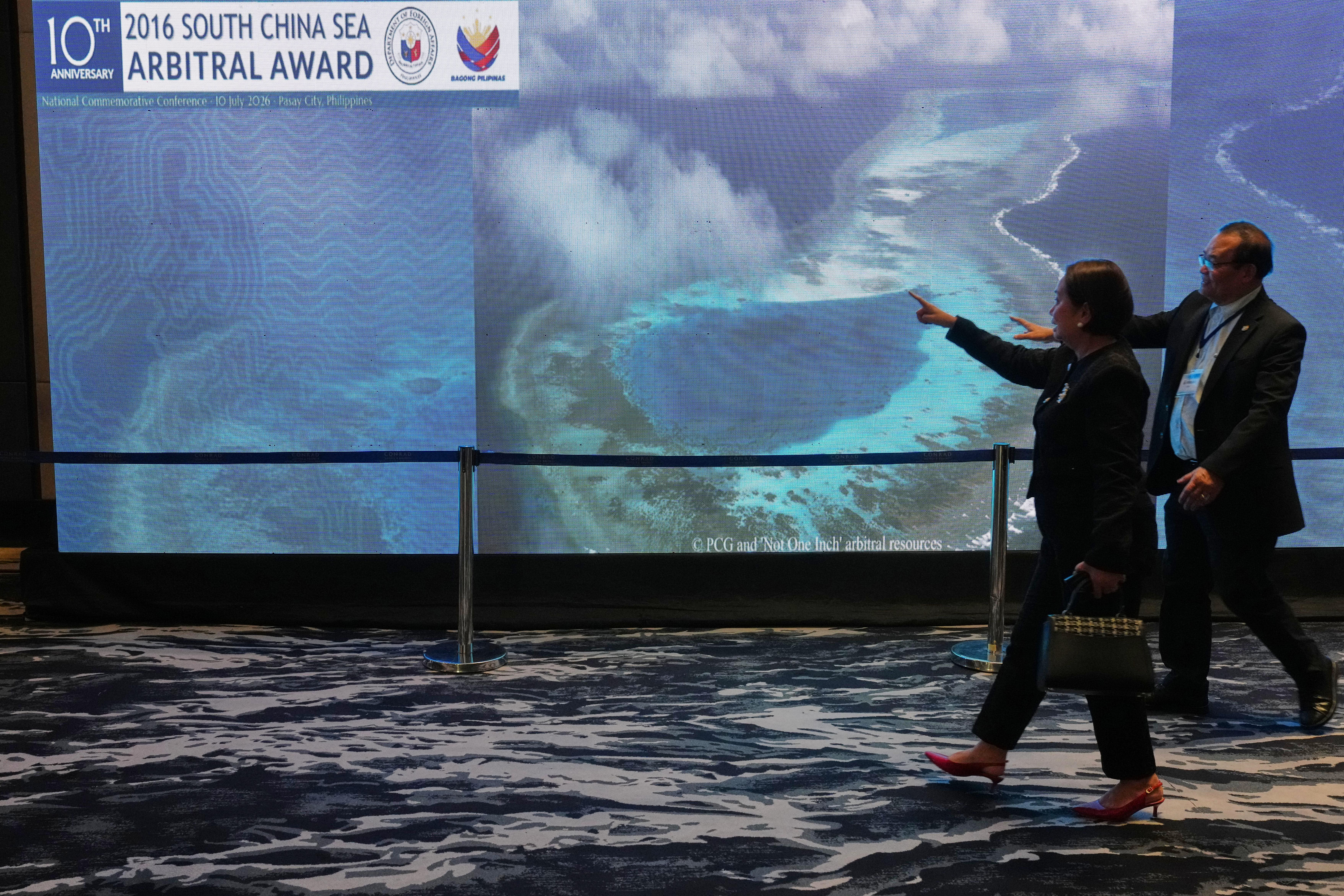 People pass by an electronic board showing areas of the disputed South China Sea (AP)
