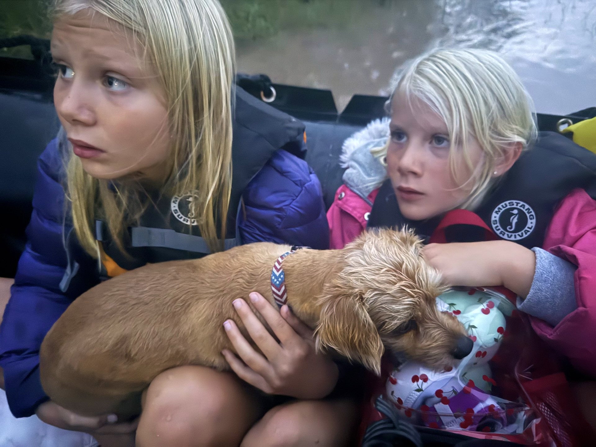 Ella and Grace Sanford and their dog Benjamin ride on a Texas Game Wardens rescue boat after being evacuated from their home after flooding in Uvalde, Texas, on Thursday
