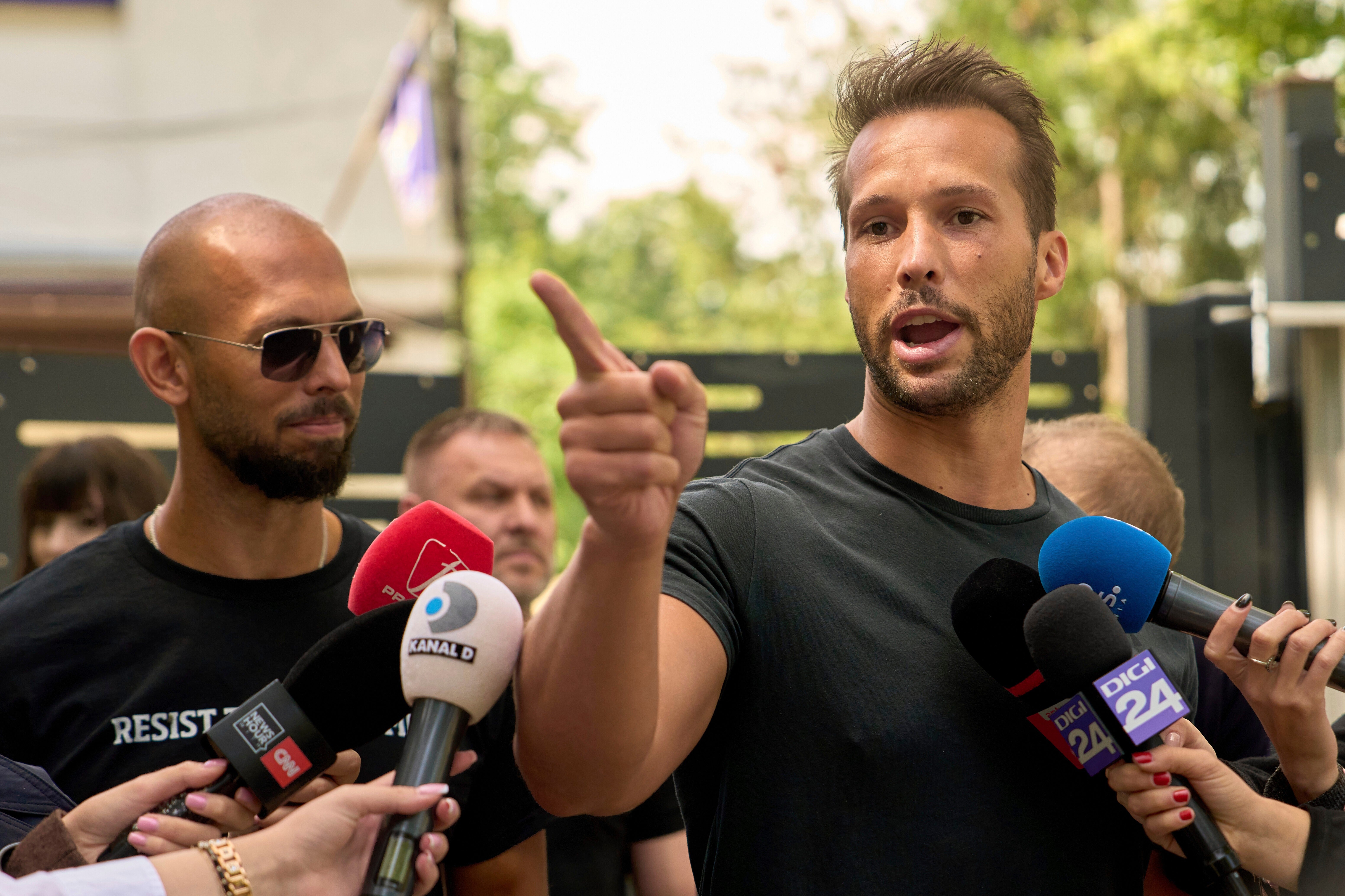 Andrew Tate, left, watches his brother Tristan speak, outside a police station in Voluntari, Romania, May 21, 2025