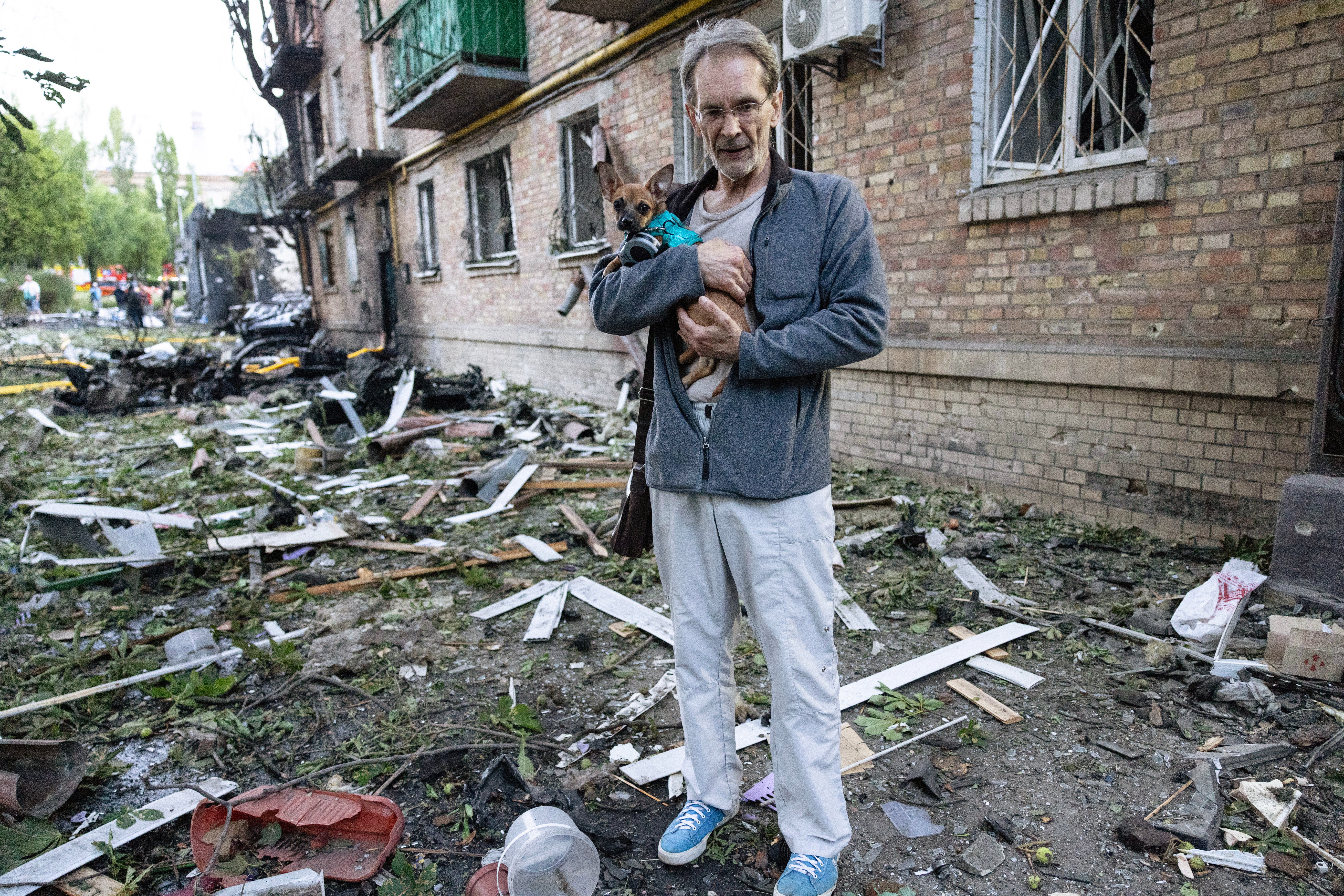 A Ukrainian man holds his dog looking at the damage to this apartment building