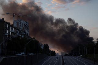 Une colonne de fumée s'élève au-dessus de la ville alors qu'une voiture roule sur une autoroute après une frappe de missile russe, alors que la Russie envahit l'Ukraine, Kiev, Ukraine, le 19 juillet 2026.