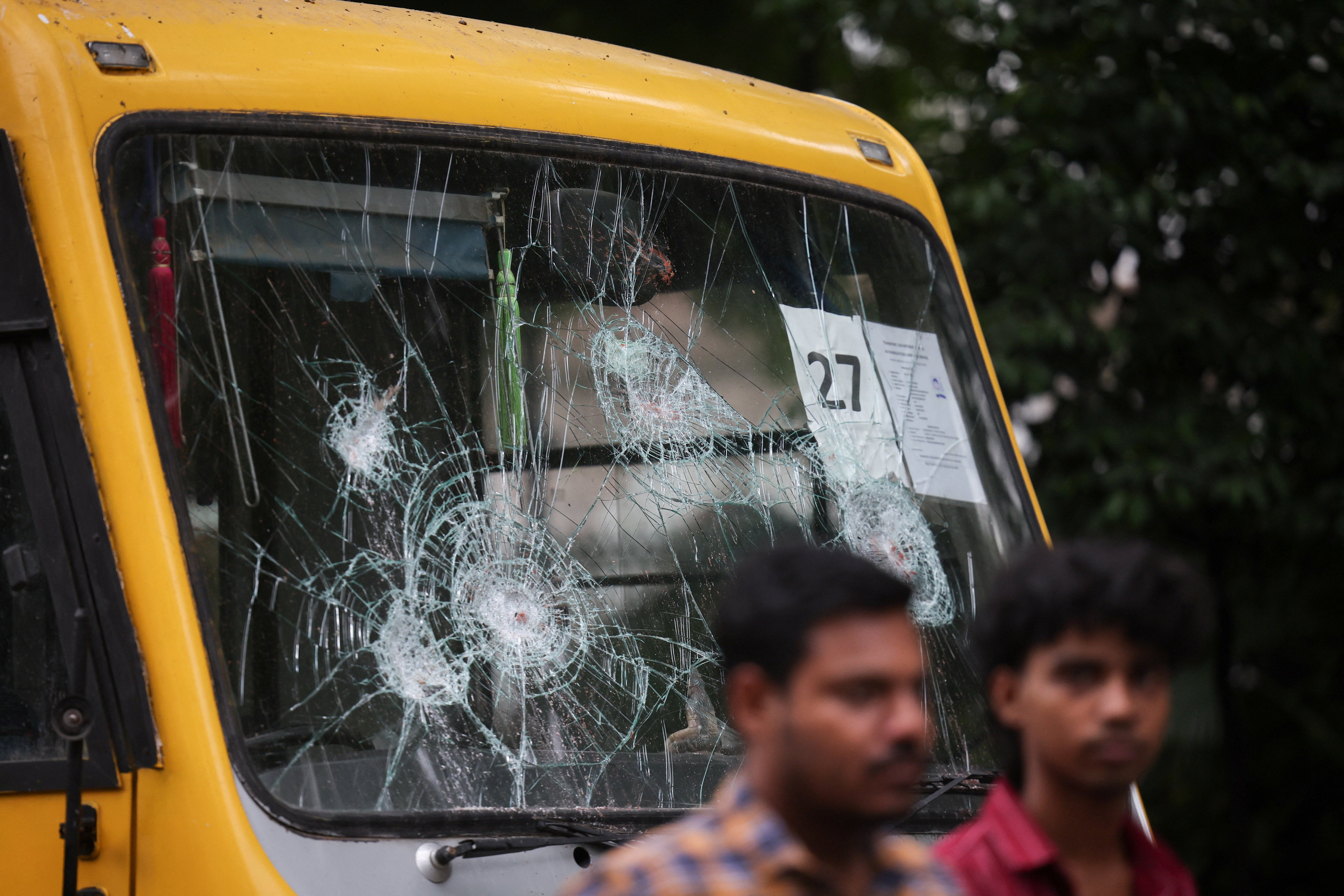 People walk next to a vandalised bus with a damaged windscreen as supporters of India's Cockroach Janta Party demonstrate