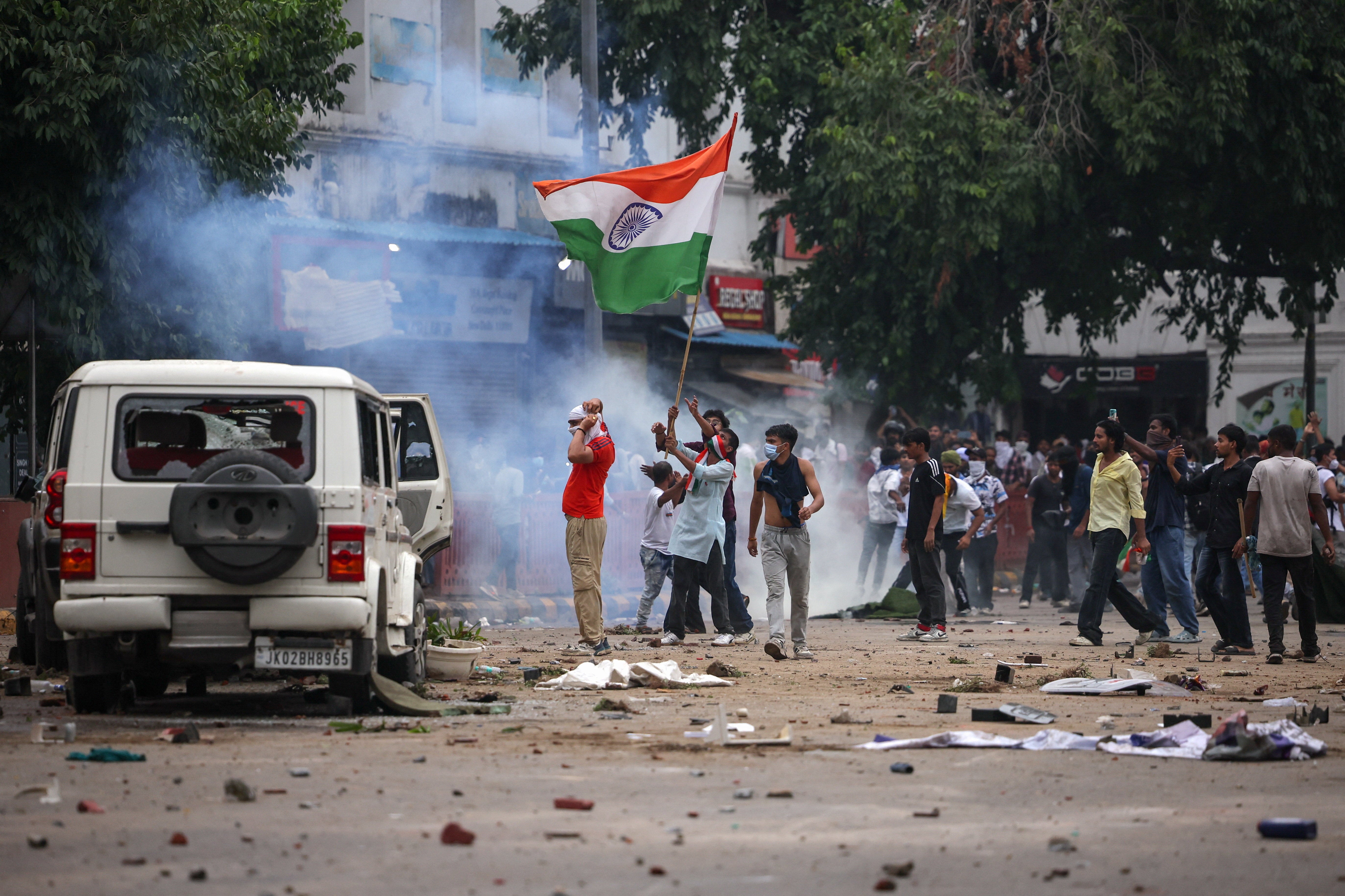 Masked protesters hold an Indian flag near plumes of tear gas