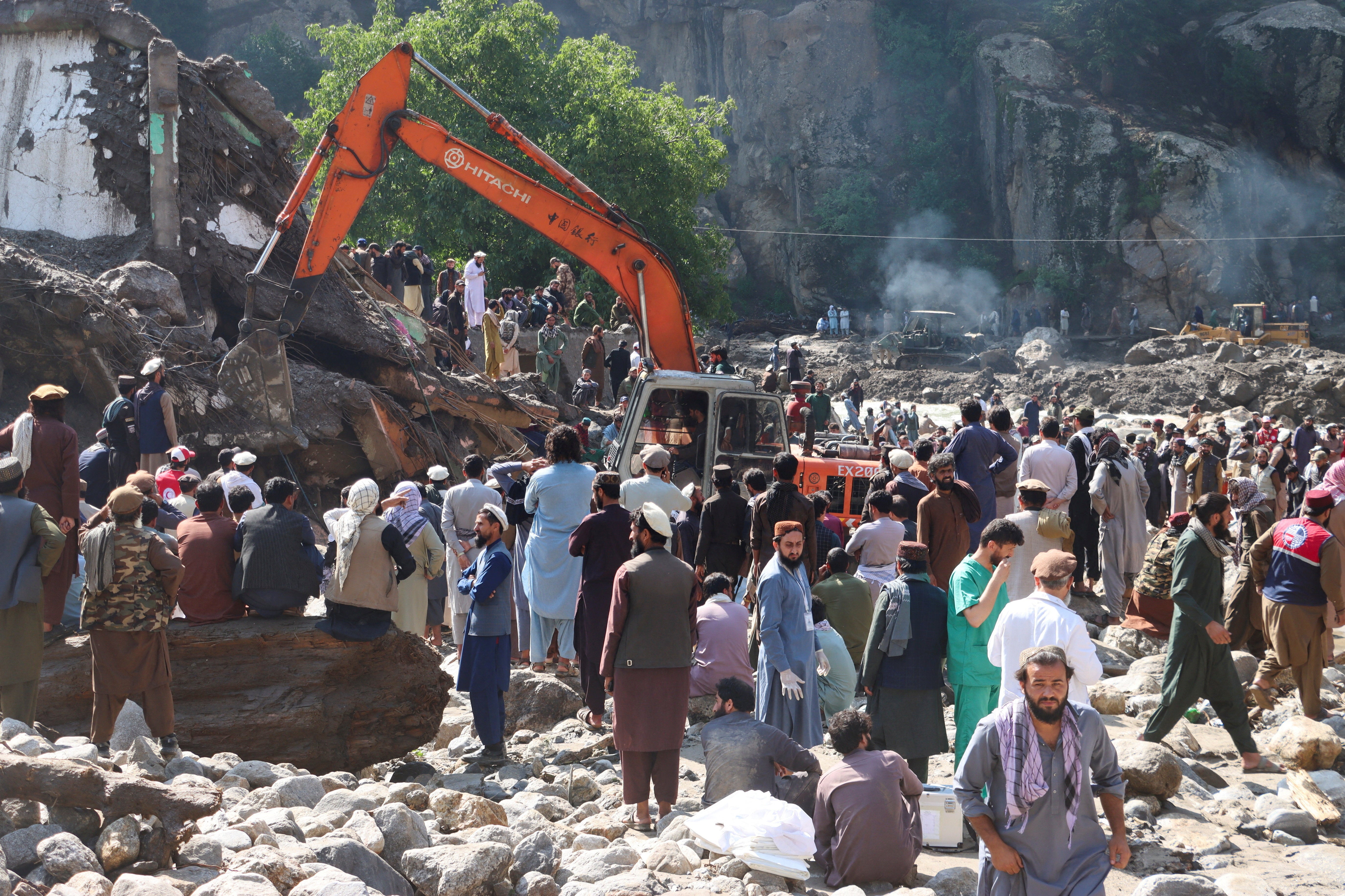 People gather as an excavator clears debris following flash floods in Parun, Nuristan, Afghanistan