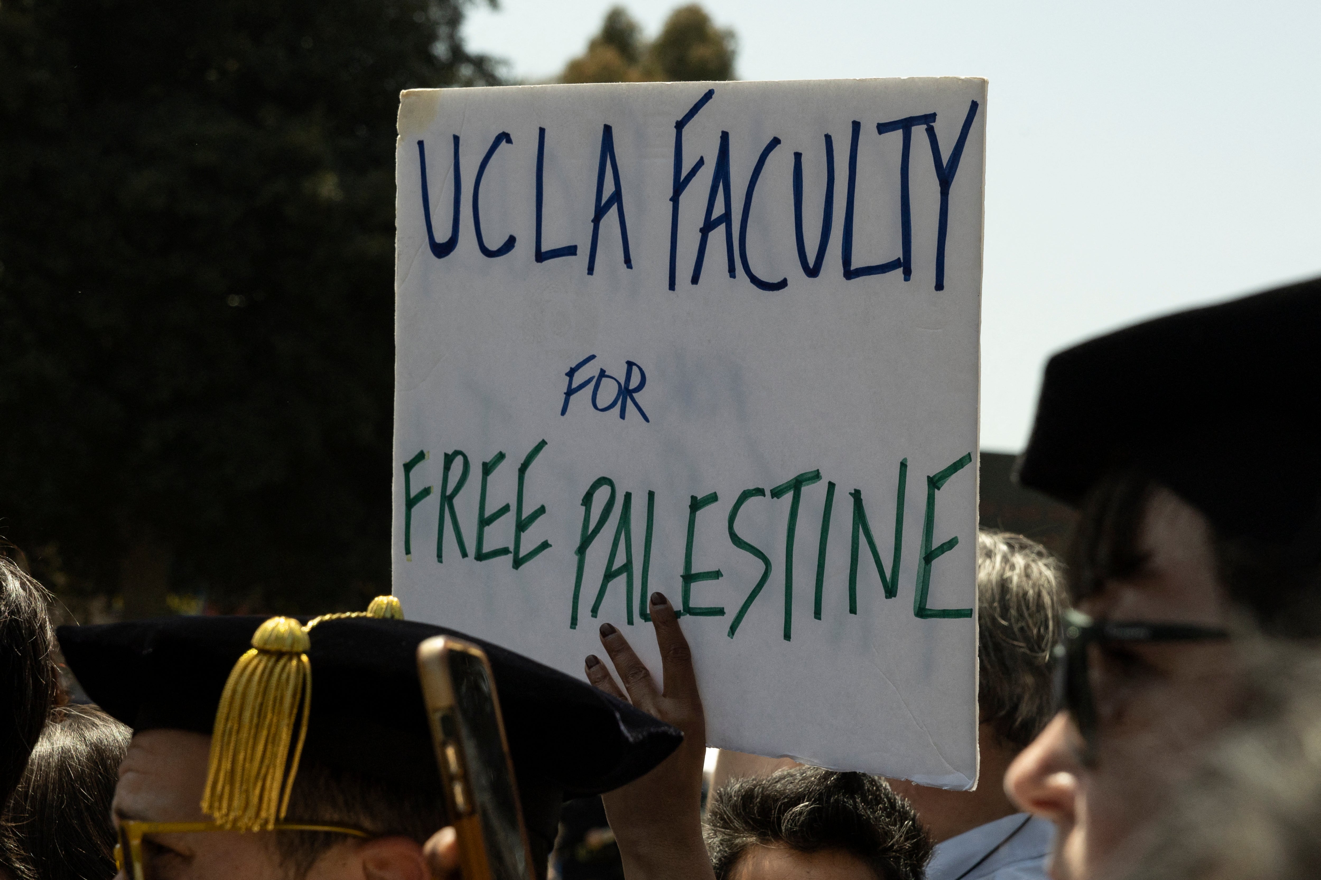 A demonstrator holds a poster reading "UCLA Faculty for Free Palestine" as UCLA faculty and staff members demonstrate next to the pro-Palestinian encampment