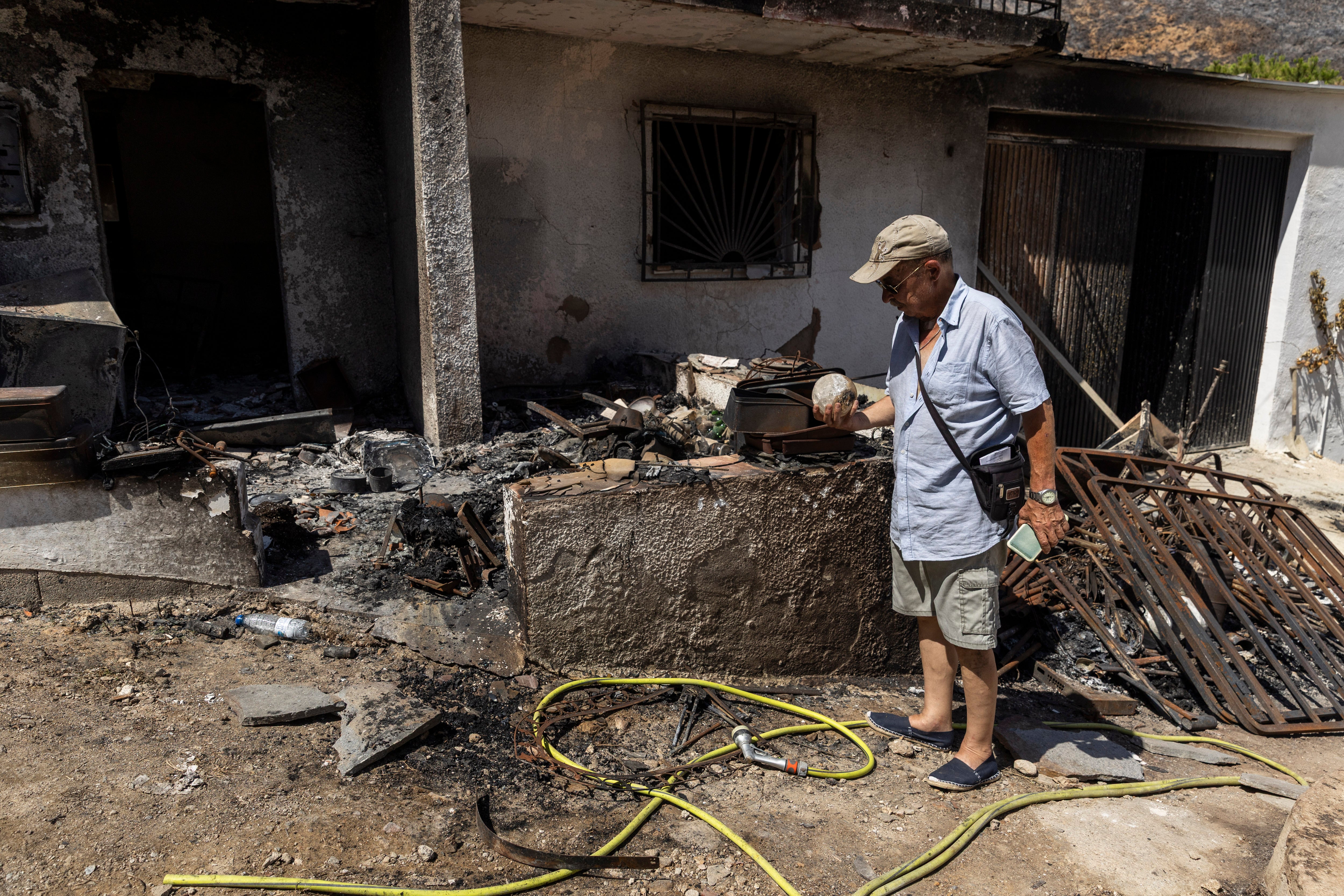 : Luis Cervera 70, checks a scorched glass ball next to his burnt house following the deadly Los Gallardos wildfire on July 13, 2026 in Fuente de la Serena, in the municipality of Bédar