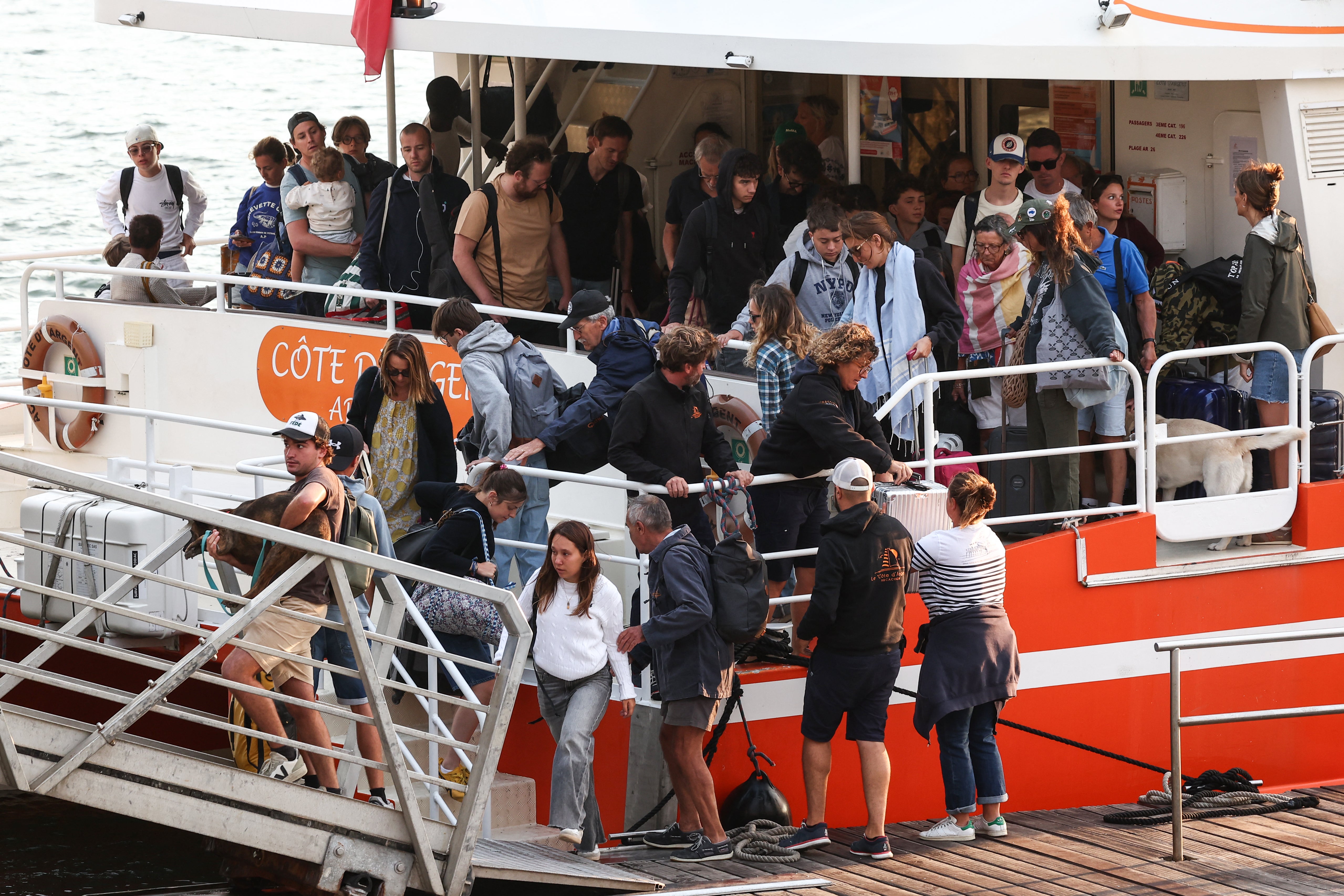 Holidaymakers from Lege-Cap-Ferret disembark from a boat upon their arrival in Arcachon during an evacuation operation of the entire Cap-Ferret peninsula