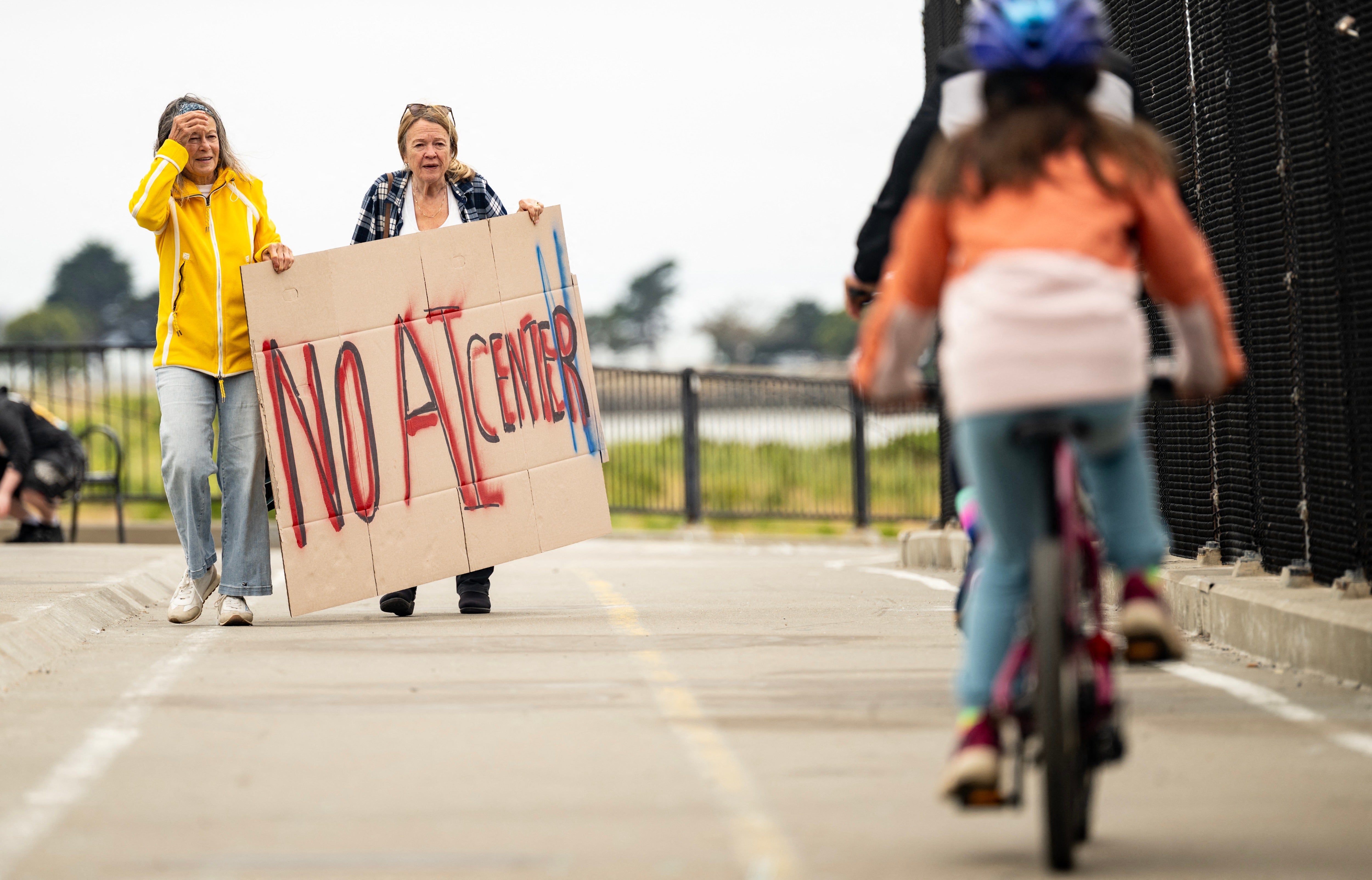 Protesters hold up signs on a pedestrian bridge during a nationwide demonstration against AI data center expansion in Berkeley, California on July 18, 2026
