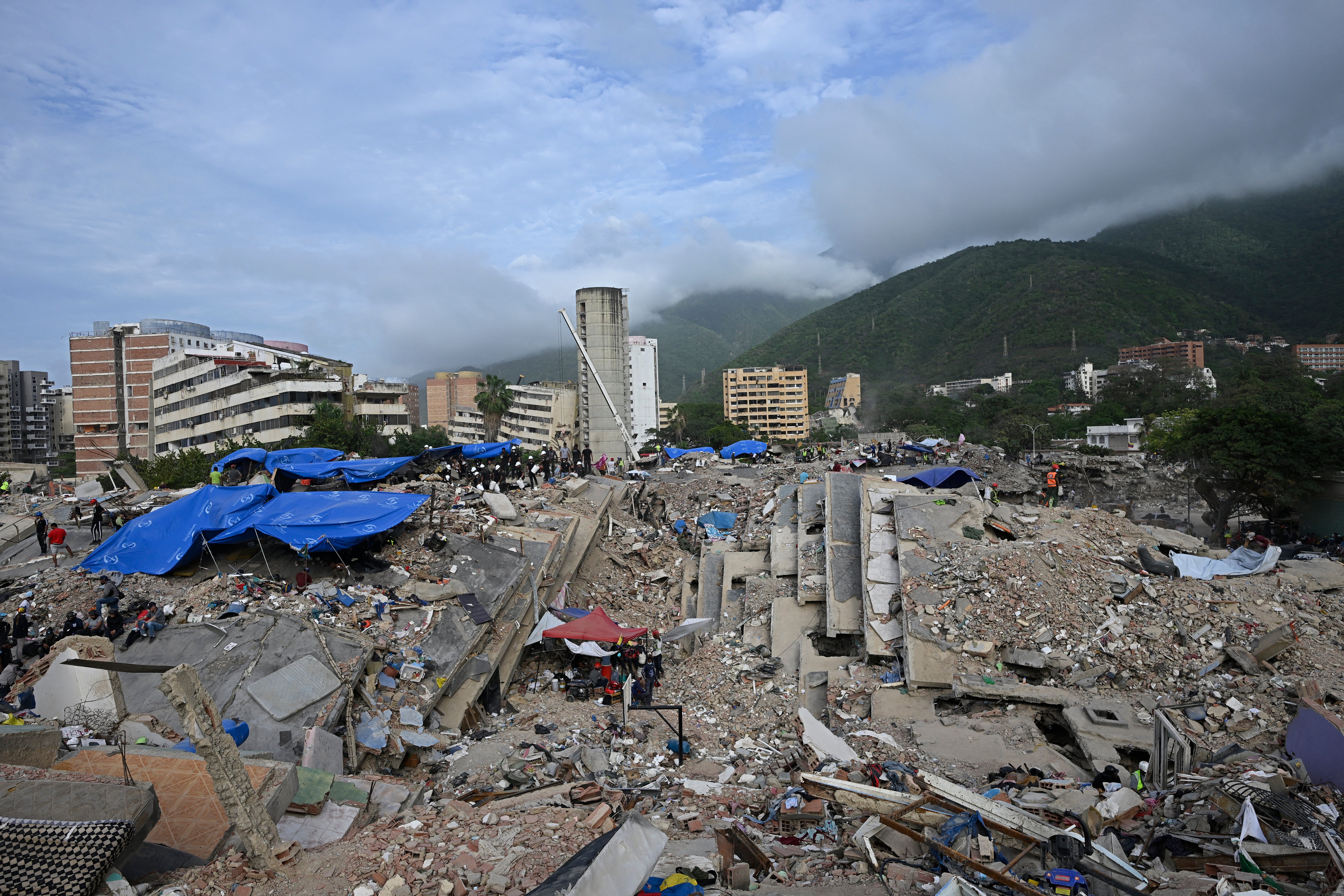 Volunteers and rescue teams still search for bodies amid the rubble of a collapsed building, nearly a month after the June 24 earthquakes