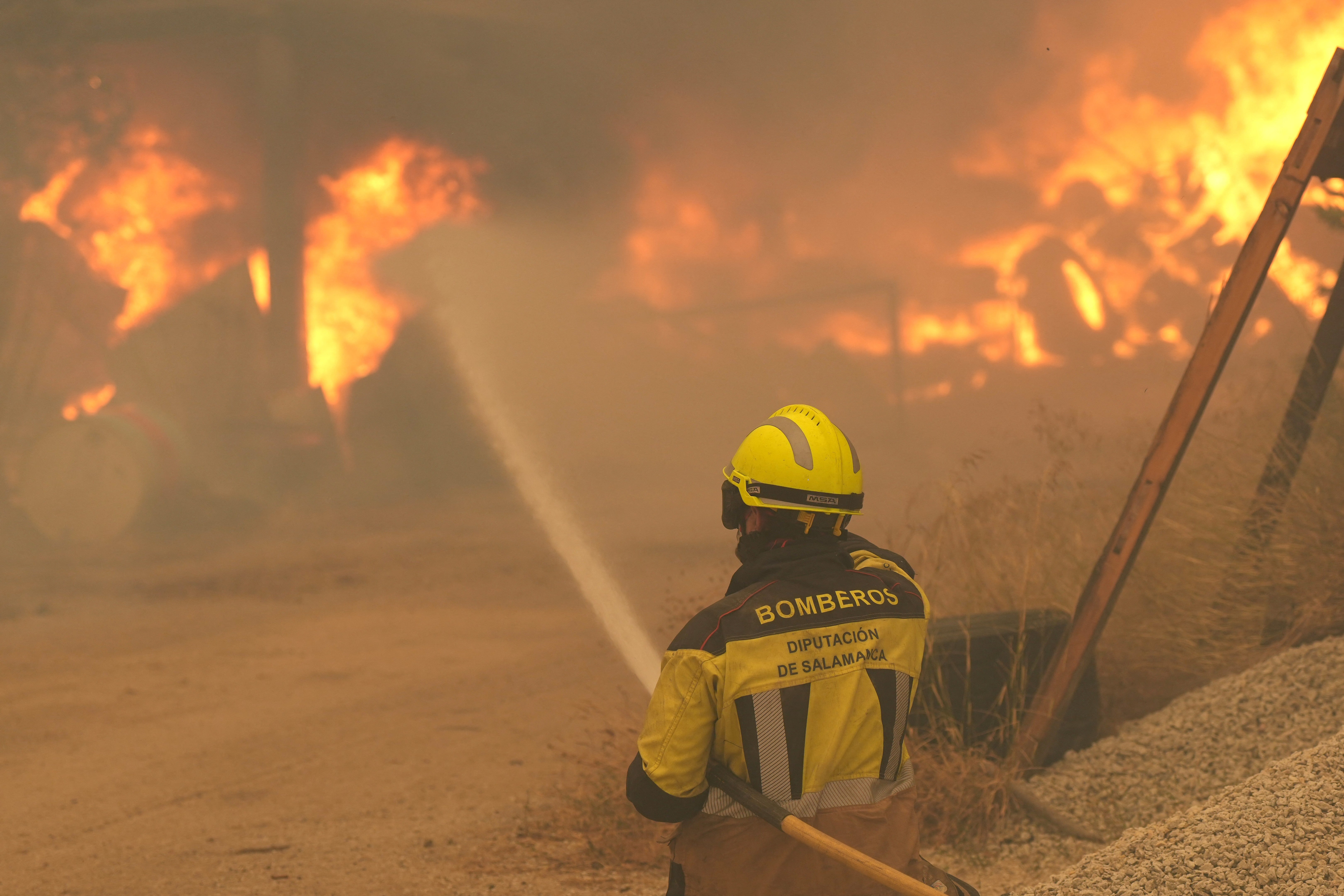 A firefighter waters burning tires and barrels while battling a wildfire in Cebreros area, near Avila, 80 kms west of Madrid on July 24, 2026. The worst wildfires in the Madrid region's history rage west of the Spanish capital, forcing authorities to evacuate or order around 40,000 people to remain indoors.