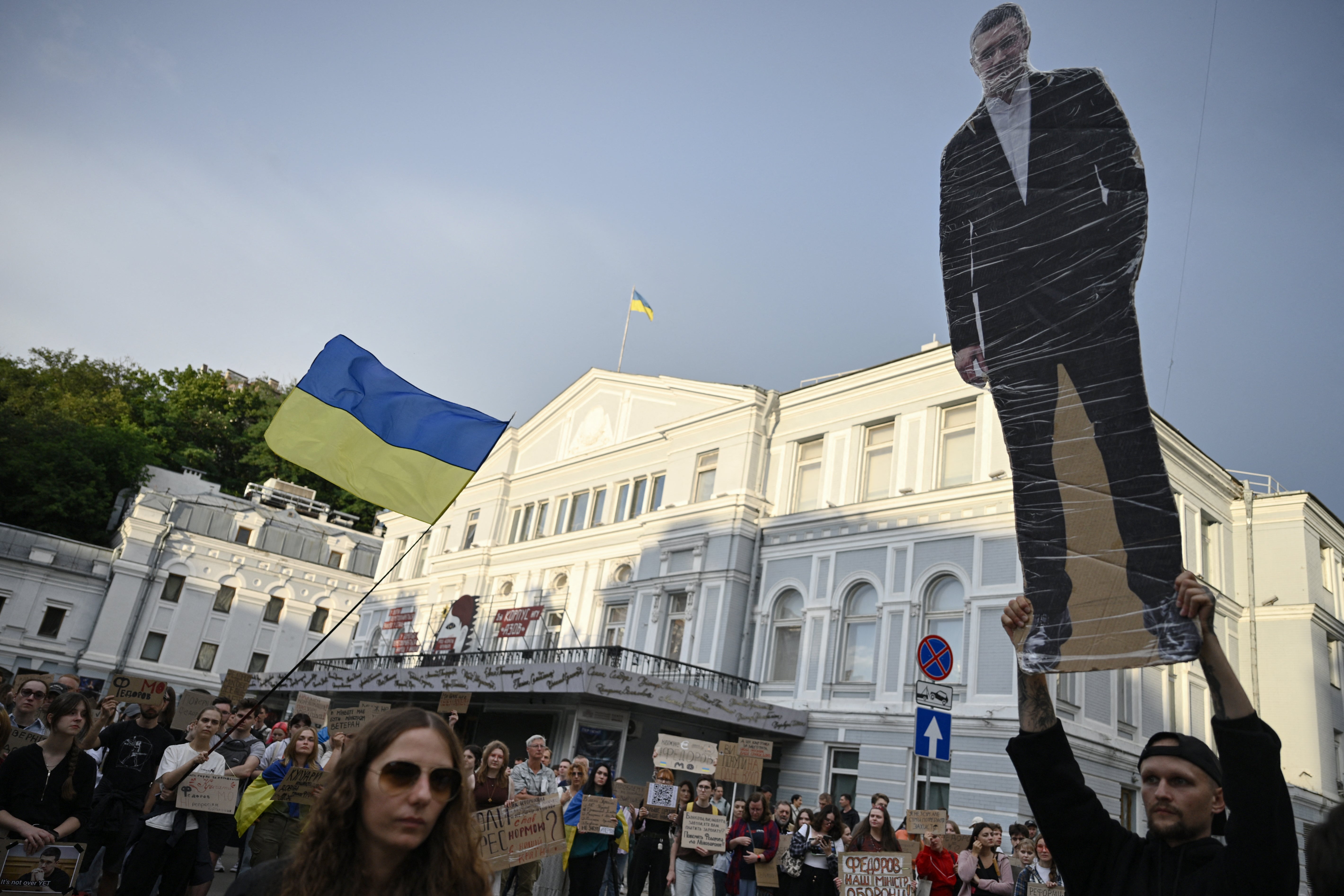 A man (R) holds a portrait placard of former defence minister Mykhailo Fedorov as people take part in a demonstration against Ukraine's President's decision in Kyiv on July 24, 2026, amid the Russian invasion of Ukraine. (AFP/Getty)