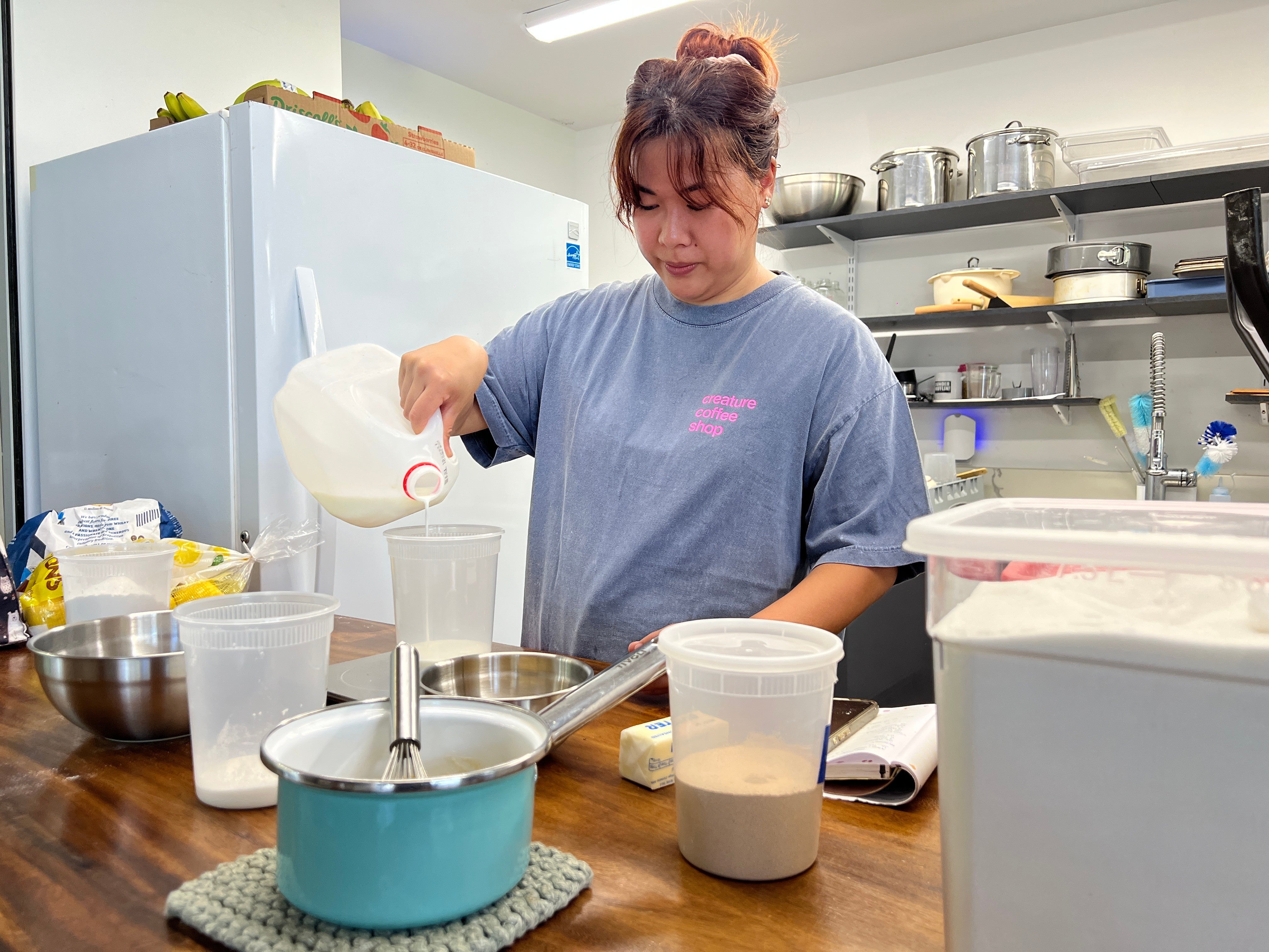 Pastry chef Amanda Tabadero pours milk into a plastic container while preparing ingredients for maritozzi at Creature Coffeeshop